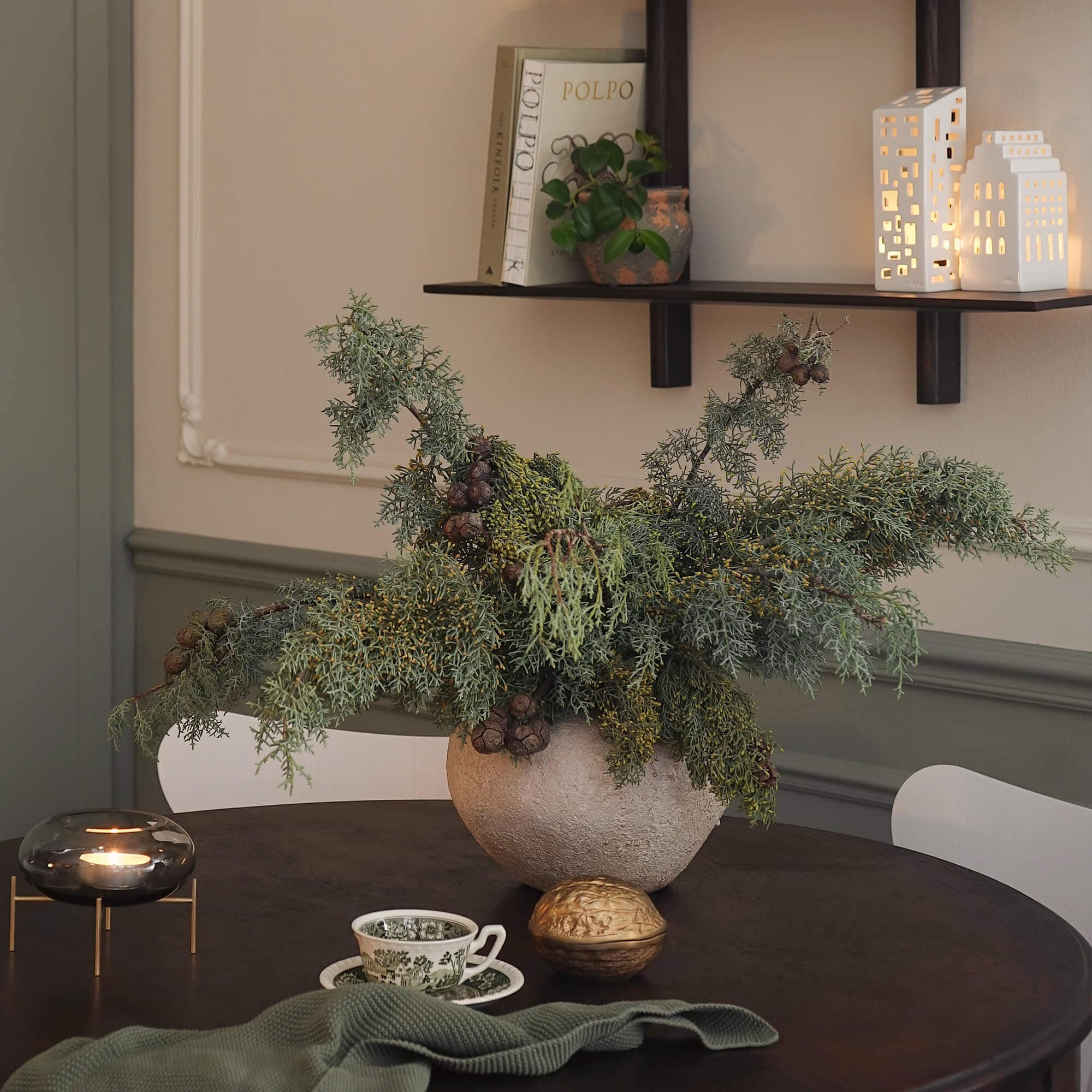 Composition décorative de branches vertes dans un pot en pierre sur une table sombre dans un salon