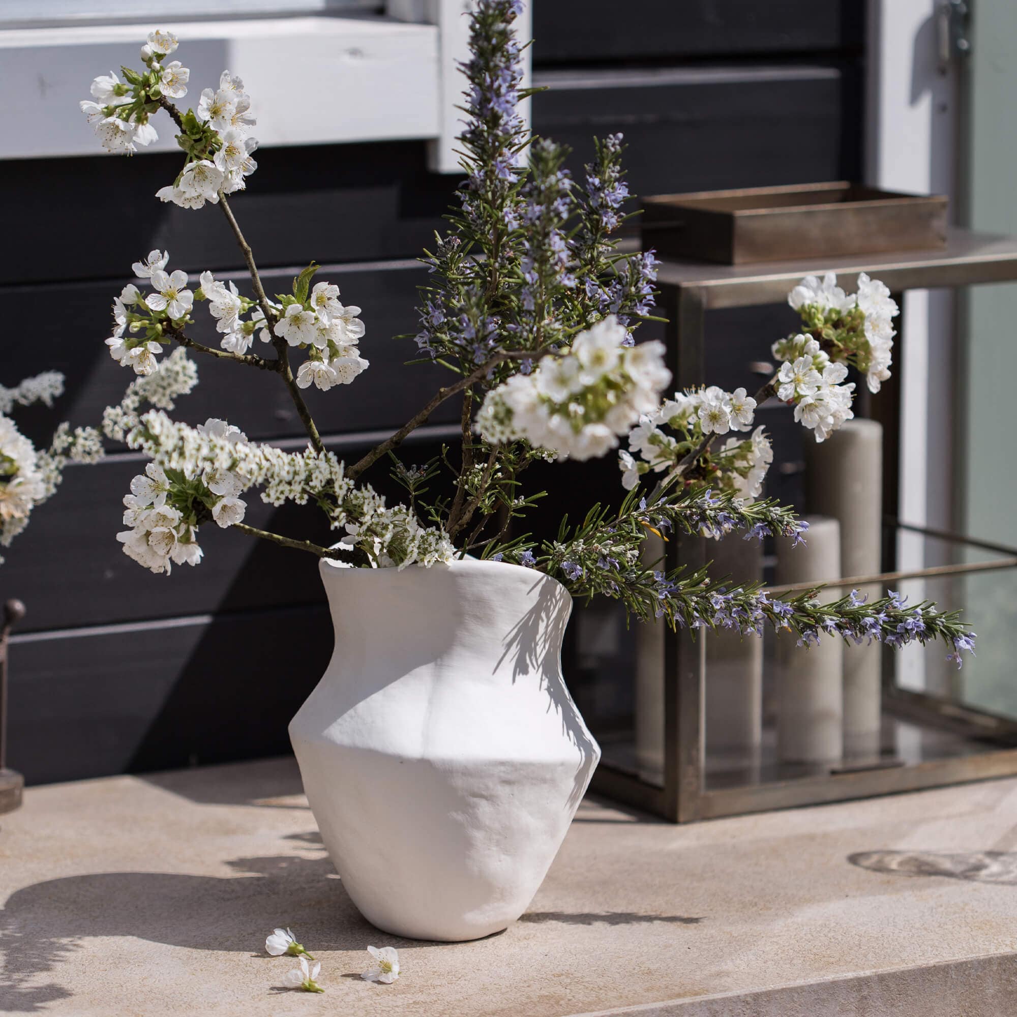 Vase en céramique blanche avec fleurs et branches sur une table extérieure décorative