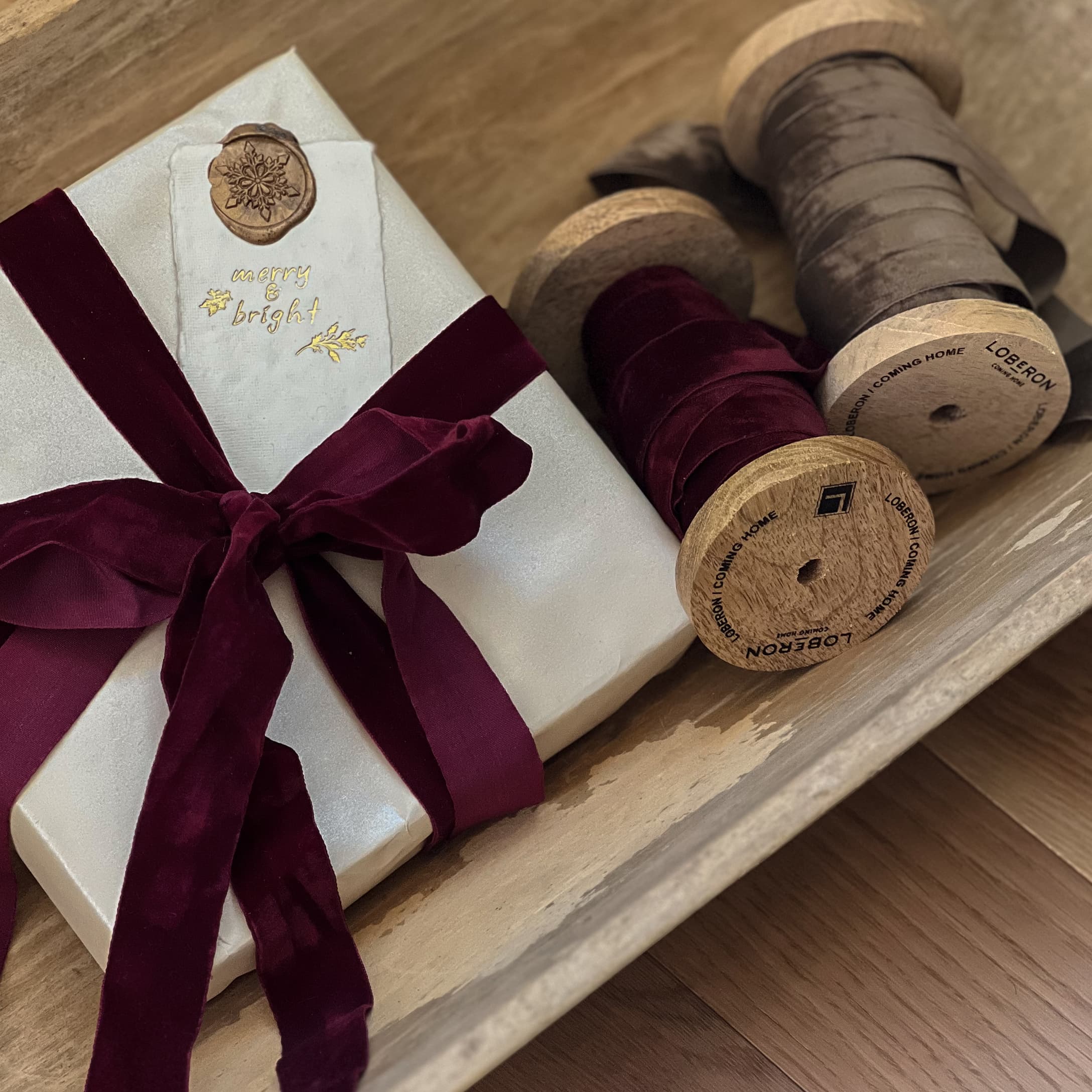 Cadeau emballé dans du papier blanc avec un ruban en velours bordeaux et bobines en bois avec rubans