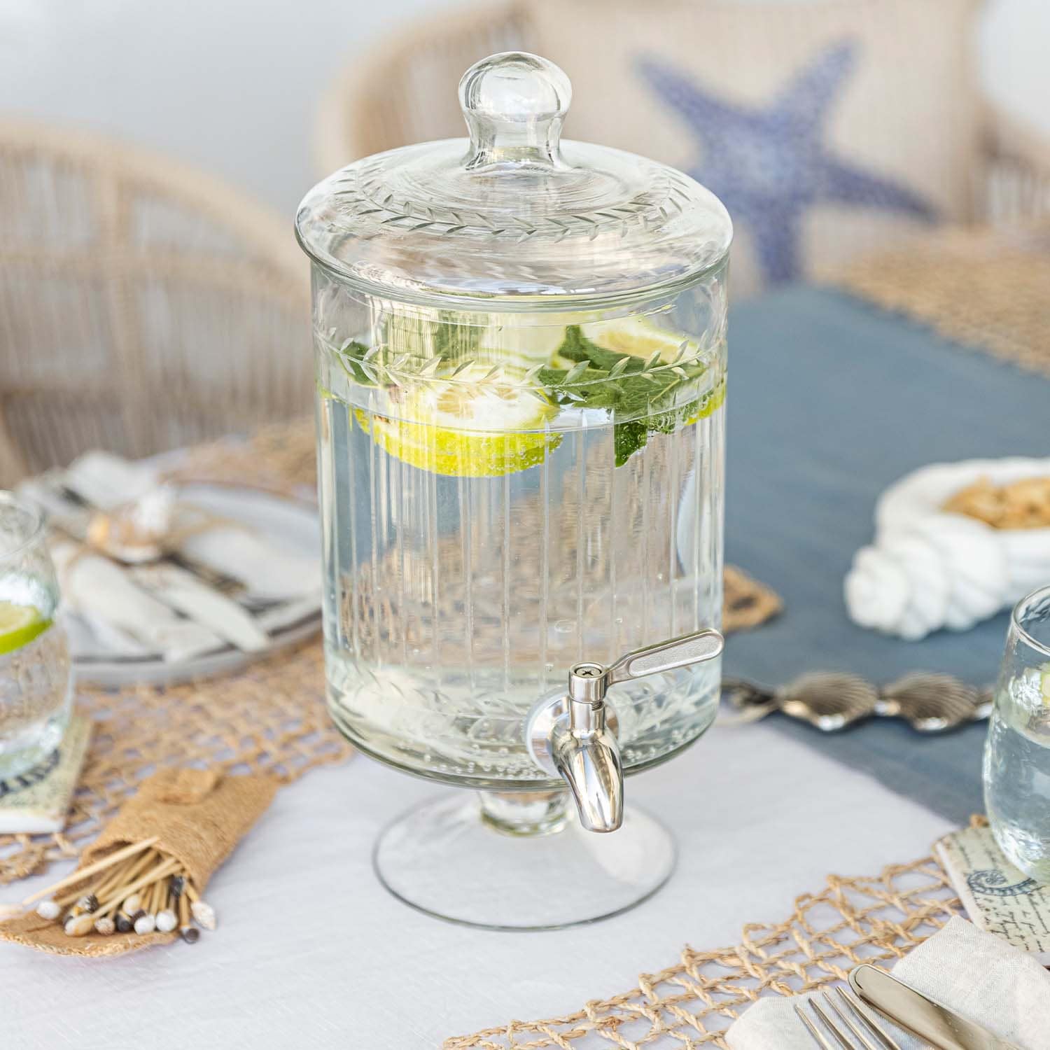 Distributeur de boissons en verre avec couvercle et robinet, eau citronnée à la menthe sur table