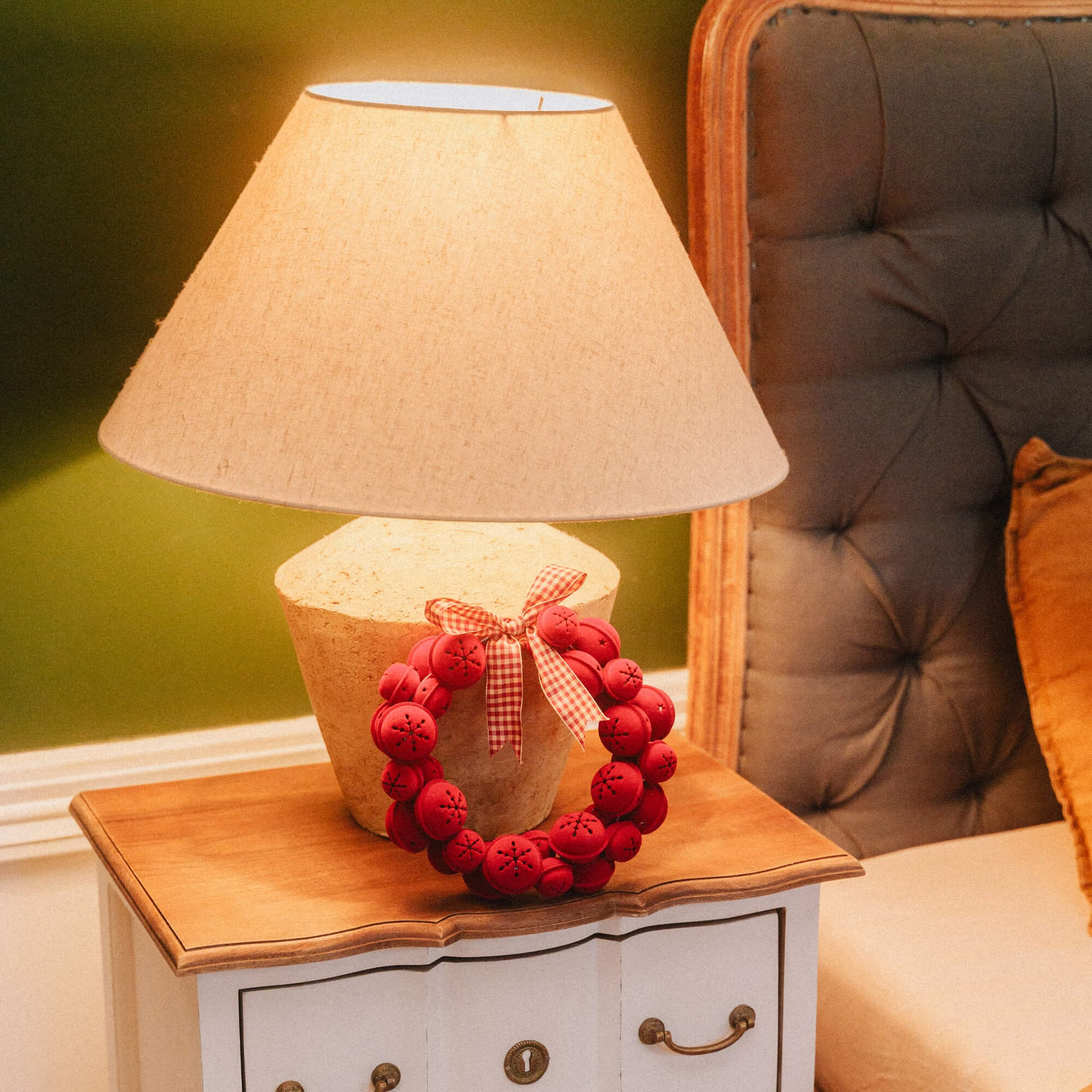 Lampe de table avec abat-jour beige et couronne de Noël rouge sur table de chevet en bois