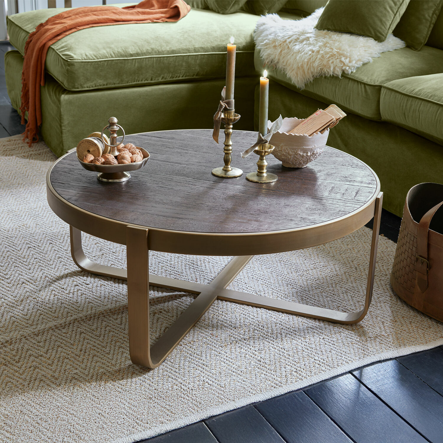 Table basse Cranthorpe Table basse ronde en bois foncé avec cadre en métal doré posée sur un tapis clair dans un salon