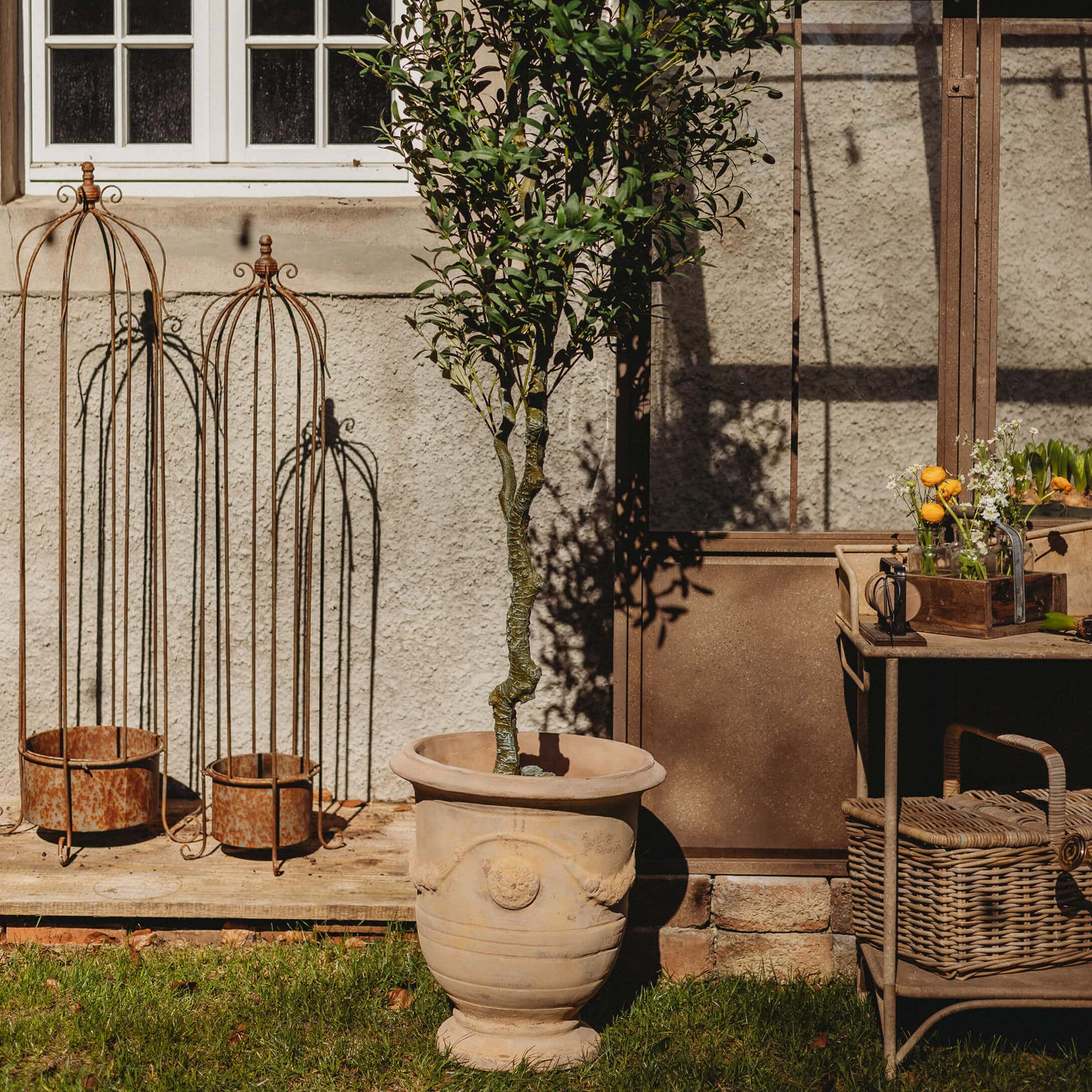Grand pot en céramique beige avec un arbre vert dans un jardin avec décorations métalliques rouillées