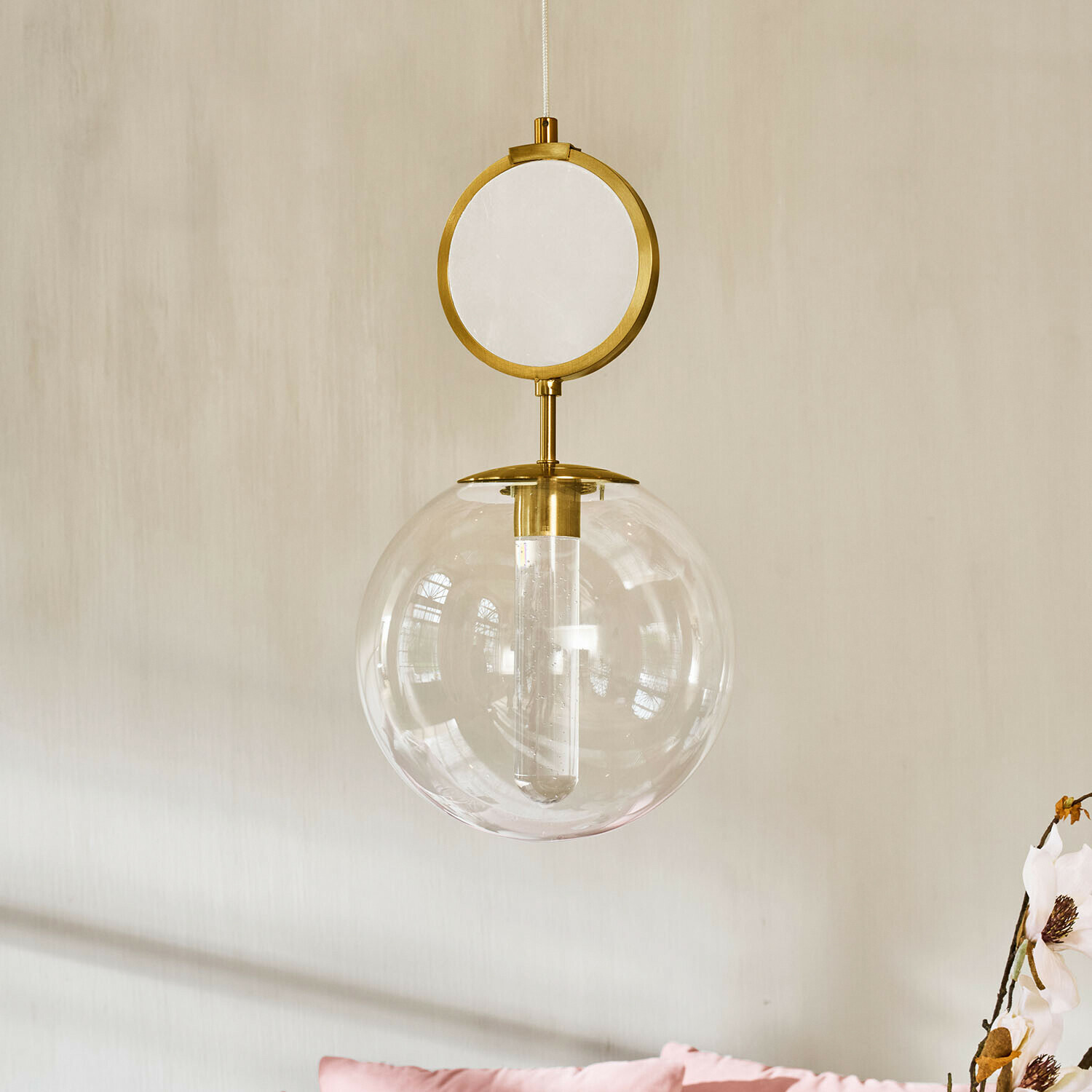 Suspension à LED Corvane Suspension dorée avec globe en verre transparent et élément circulaire décoratif sur fond de mur clair