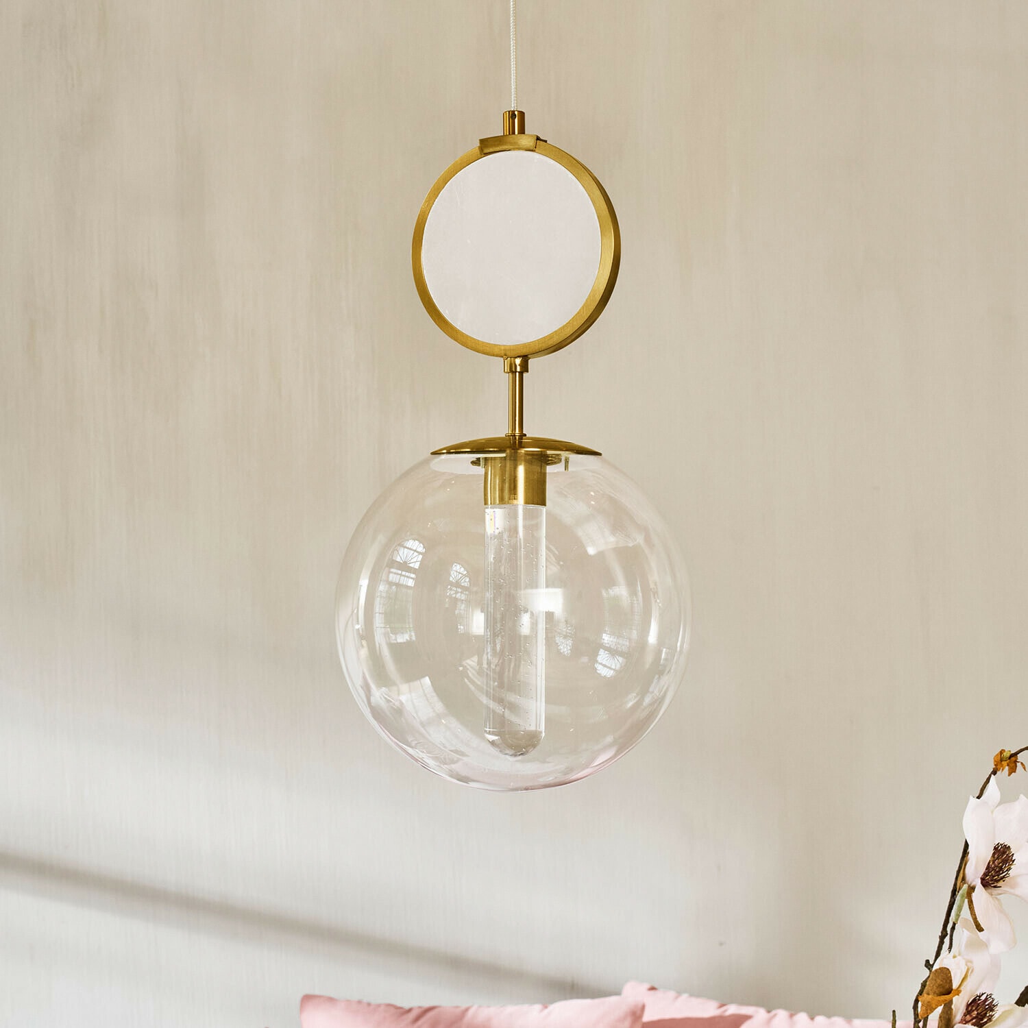 Suspension à LED Corvane Suspension dorée avec globe en verre transparent et élément circulaire décoratif sur fond de mur clair