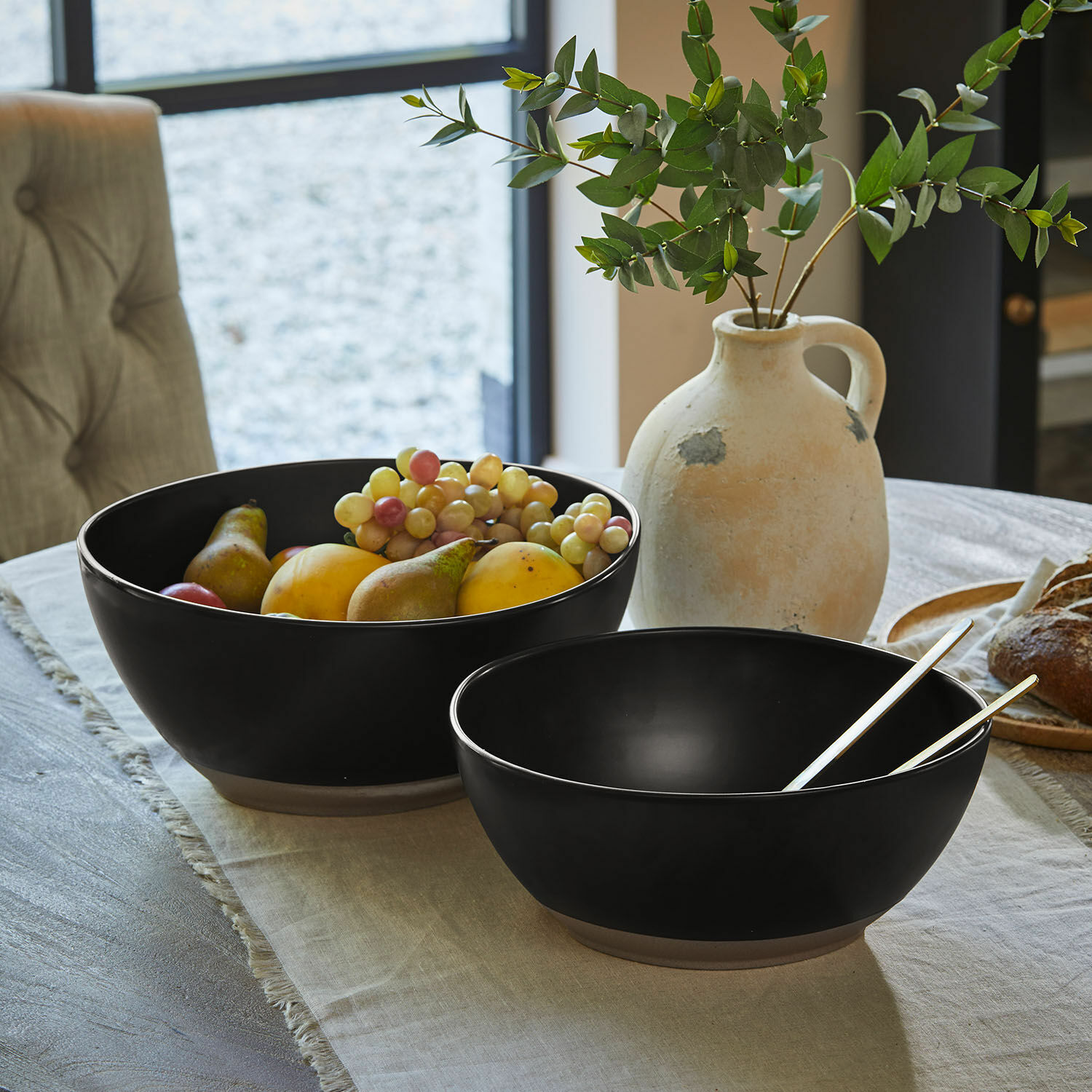 Lot de 2 saladiers Biarré Deux bols en céramique noire remplis de légumes verts sur une table en bois clair