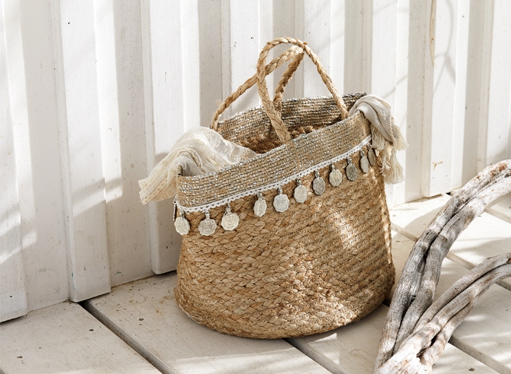 Panier bohème en matériau naturel tressé avec pièces décoratives et foulard clair, décoration intérieure.