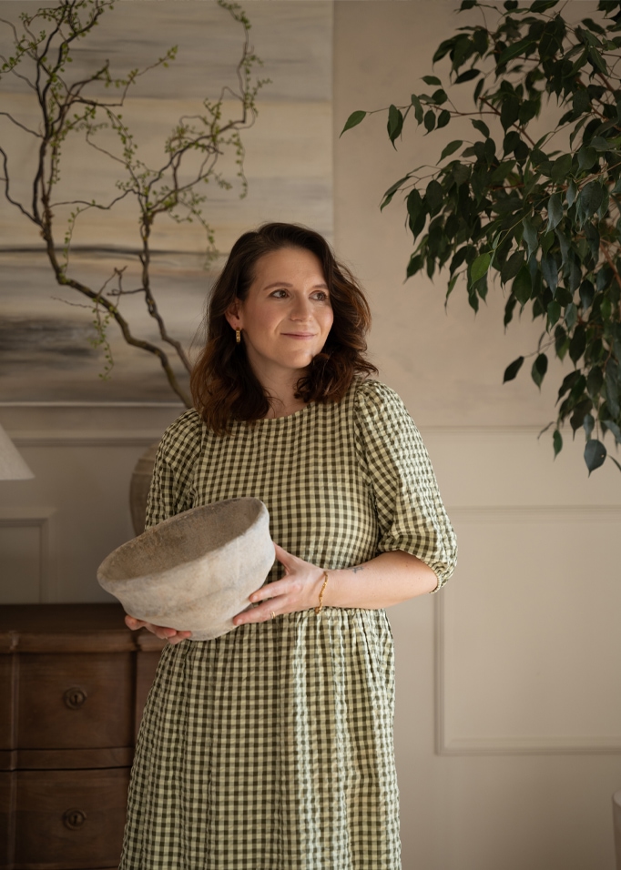 Femme en robe à carreaux verts tenant un bol en céramique grise dans un intérieur chaleureux