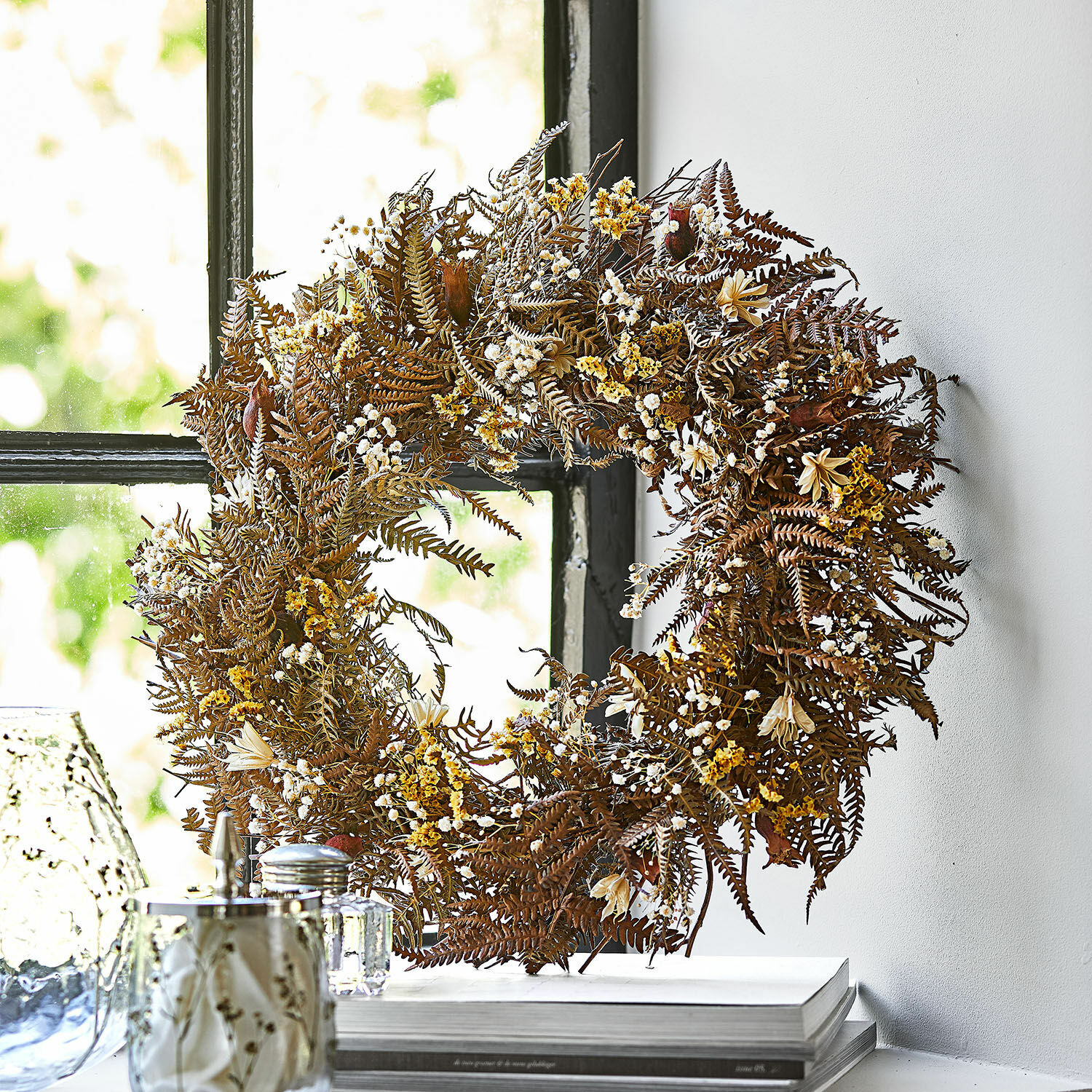 Couronne de fleurs séchées Evique Couronne décorative en fougères séchées et fleurs jaunes et brunes posée sur une fenêtre