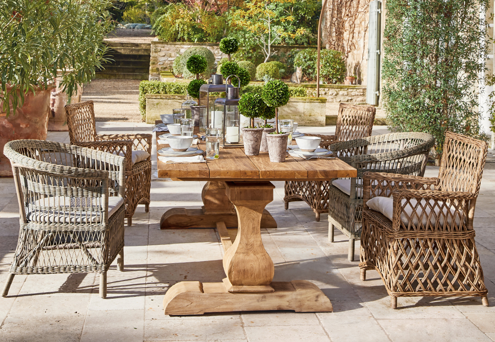 Table de jardin en bois avec chaises en osier et décorations végétales sur terrasse au style méditerranéen