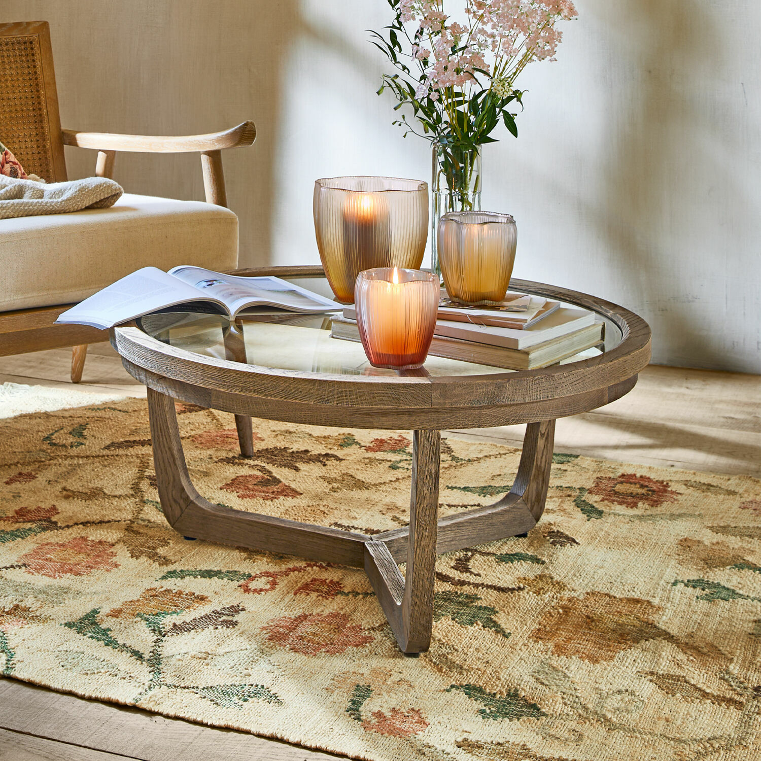 Table basse Gradn Enclos Table basse ronde en bois et verre sur tapis fleuri avec bougies et livres décoratifs
