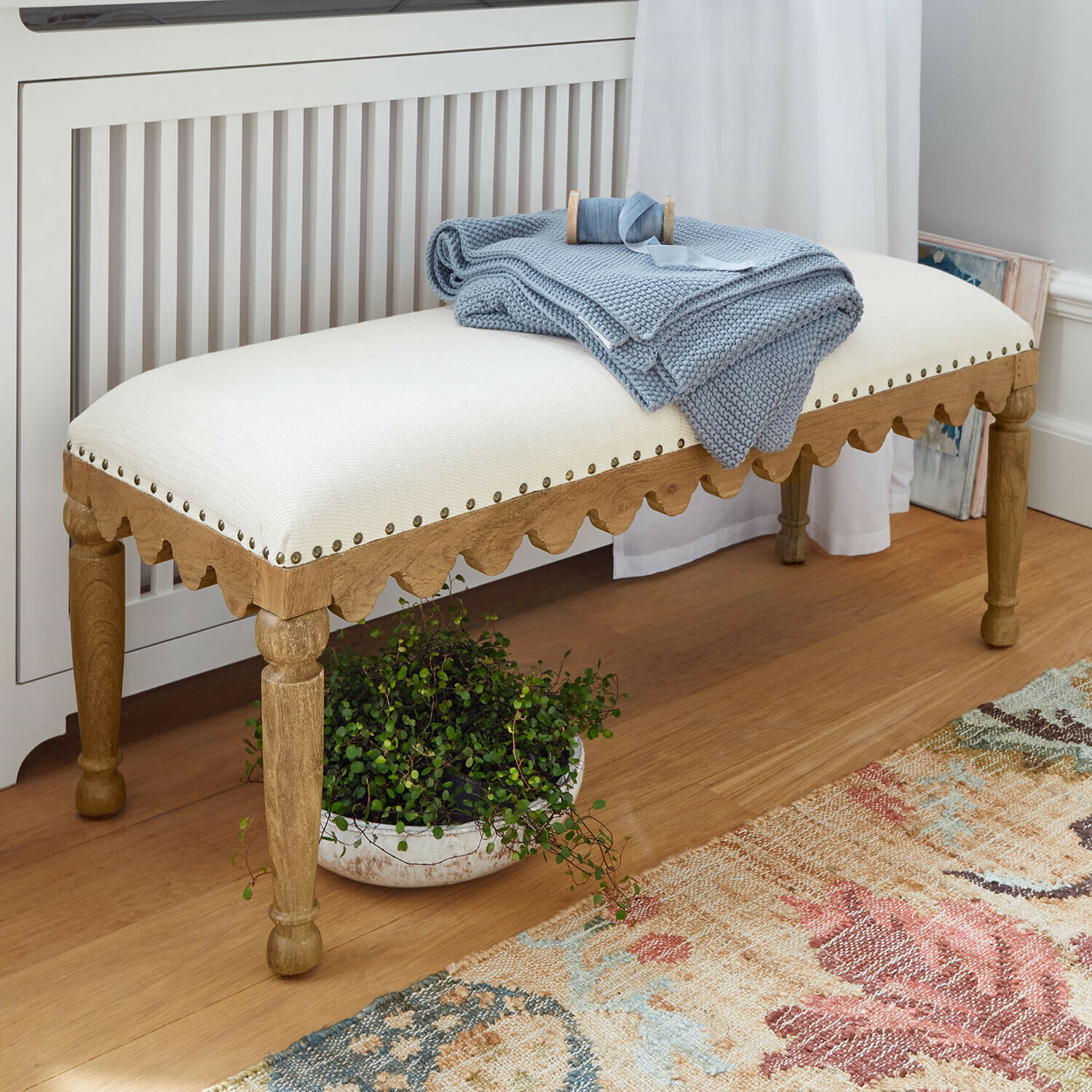 Banquette Marais Légère Banc en bois clair avec assise crème et plaid bleu posé dessus dans un intérieur chaleureux
