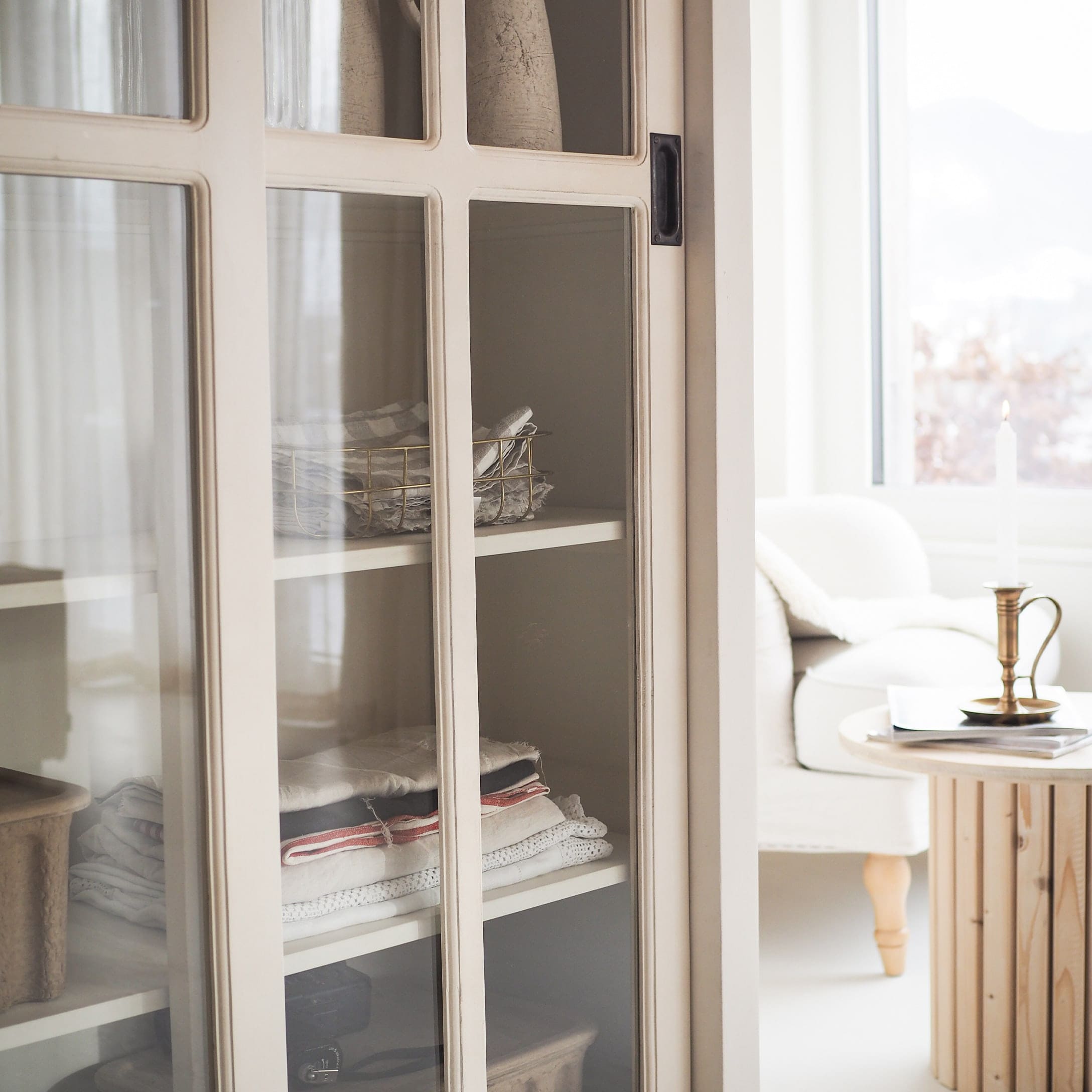 Armoire en bois blanc avec portes vitrées et tissus pliés dans un intérieur lumineux