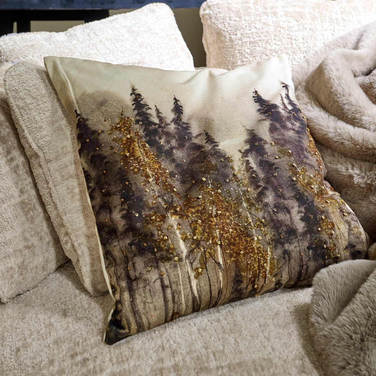 Housse de coussin Aurignac Coussin décoratif avec motif forêt et sequins dorés sur tissu beige posé sur canapé