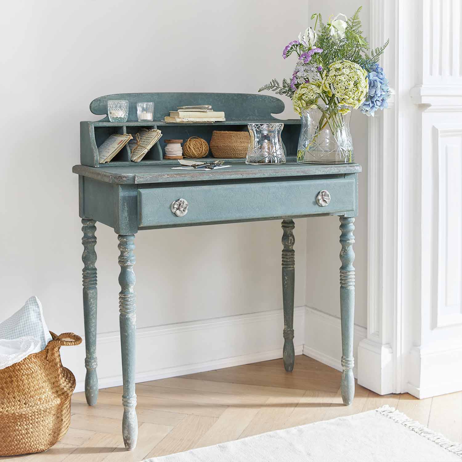 Bureau en bois bleu avec tiroir et étagères, décoré d'un vase fleuri et de bougies