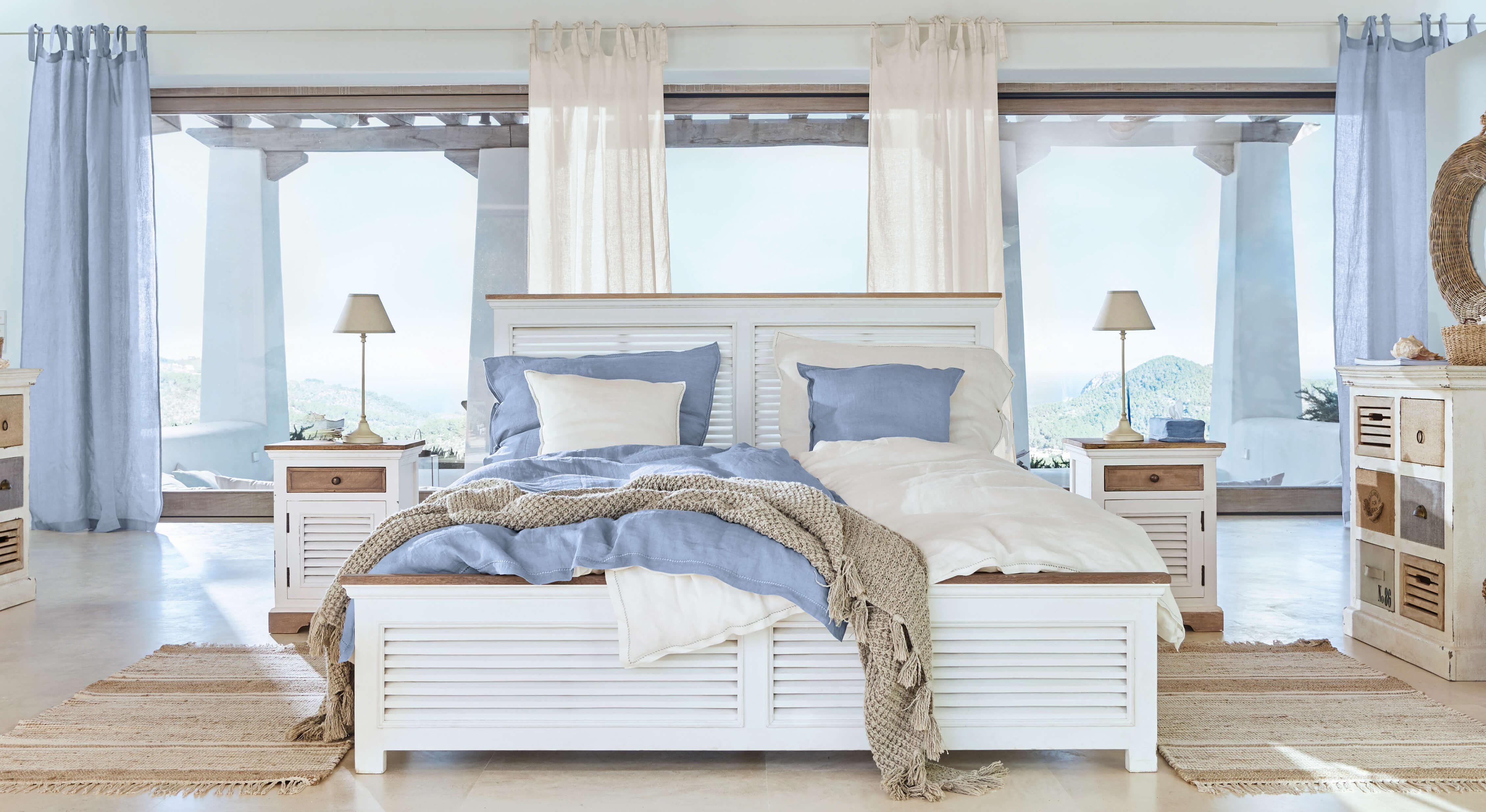 Lit en bois blanc avec literie bleu et beige, tapis naturel dans chambre lumineuse avec vue panoramique