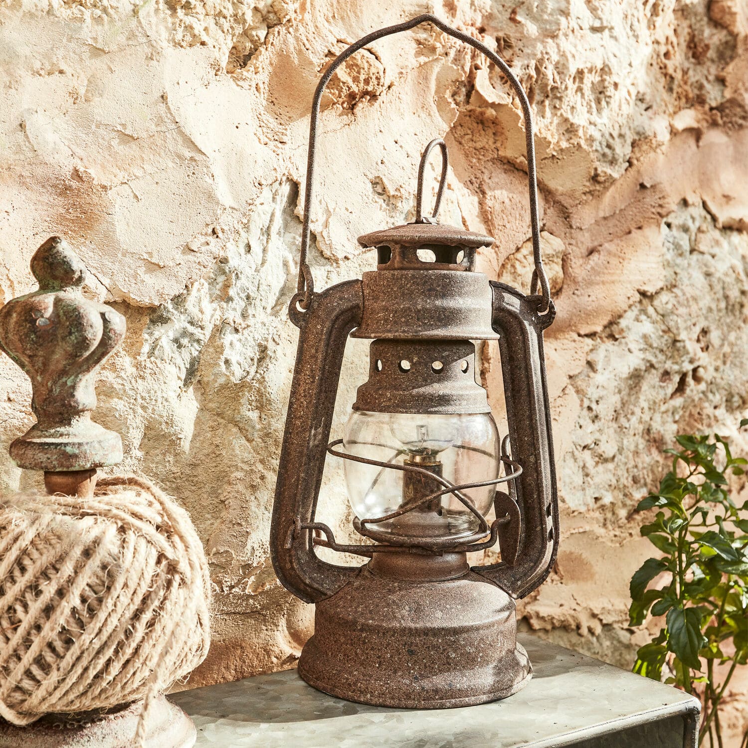 Lanterne LED Oxcroft Lampe à pétrole en métal rouillé de style rustique posée devant un mur en pierre, décoration vintage