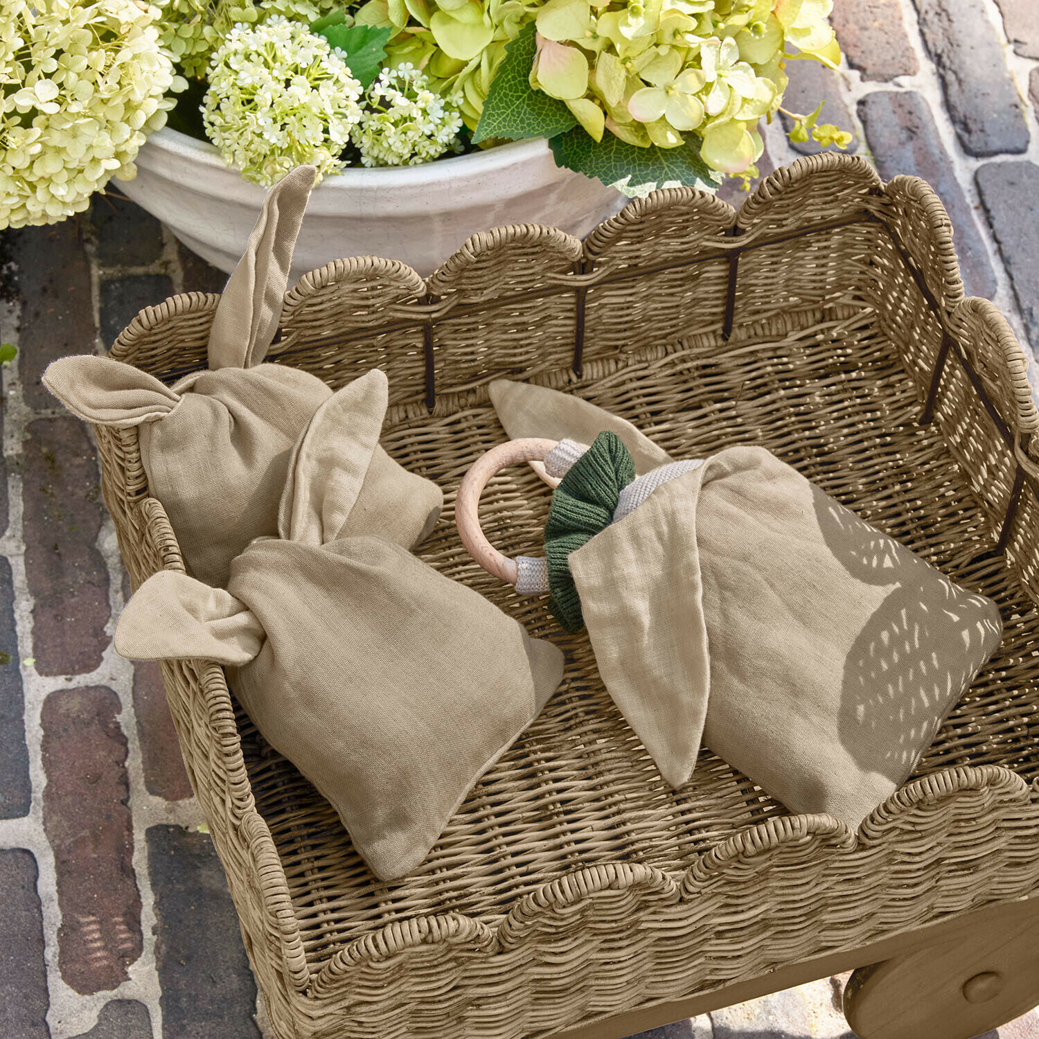 Set de 3 sacs Snugglewood Sac en lin beige avec oreilles dans un panier en osier, décor floral et sol en briques