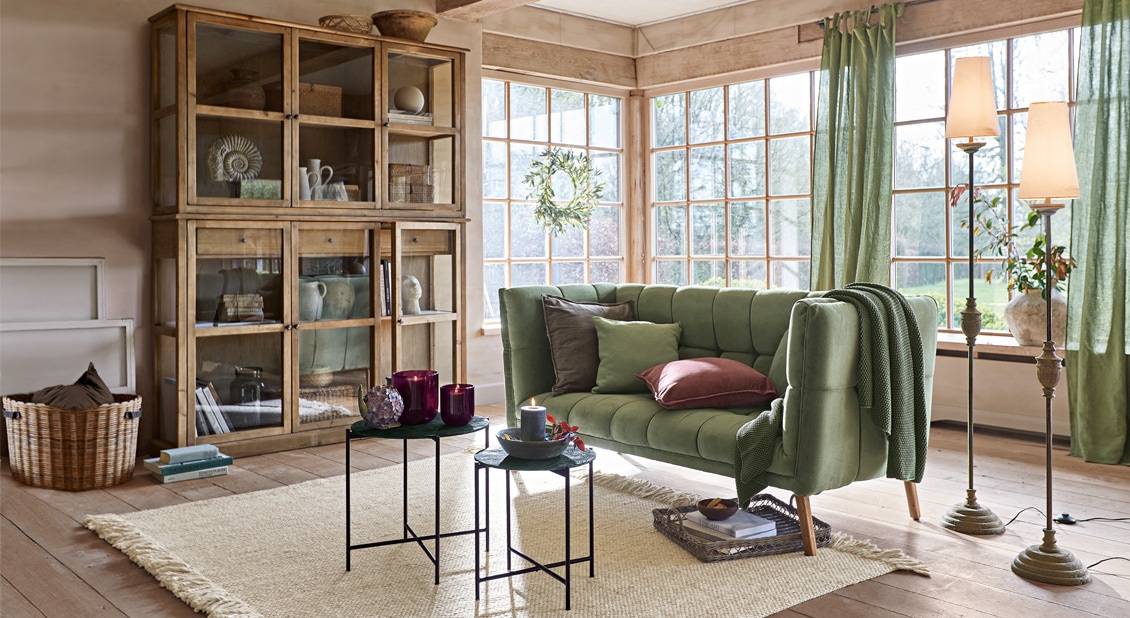 Salon chaleureux avec canapé vert en tissu, vitrine en bois et tapis naturel sur le sol en bois