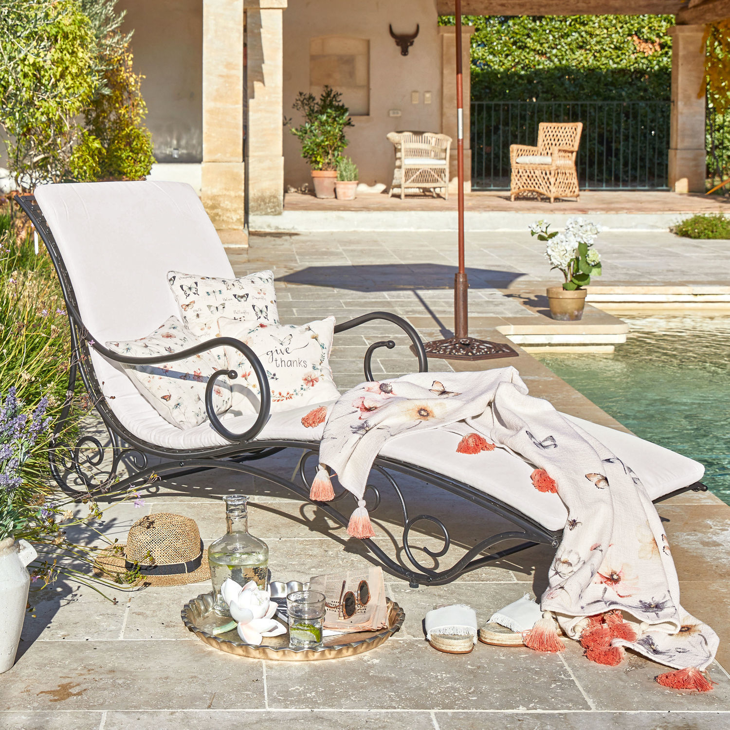 Matelas de chaise longue Turballe Chaise longue de jardin en métal noir avec coussins clairs et plaid à motifs floraux et papillons près de la piscine