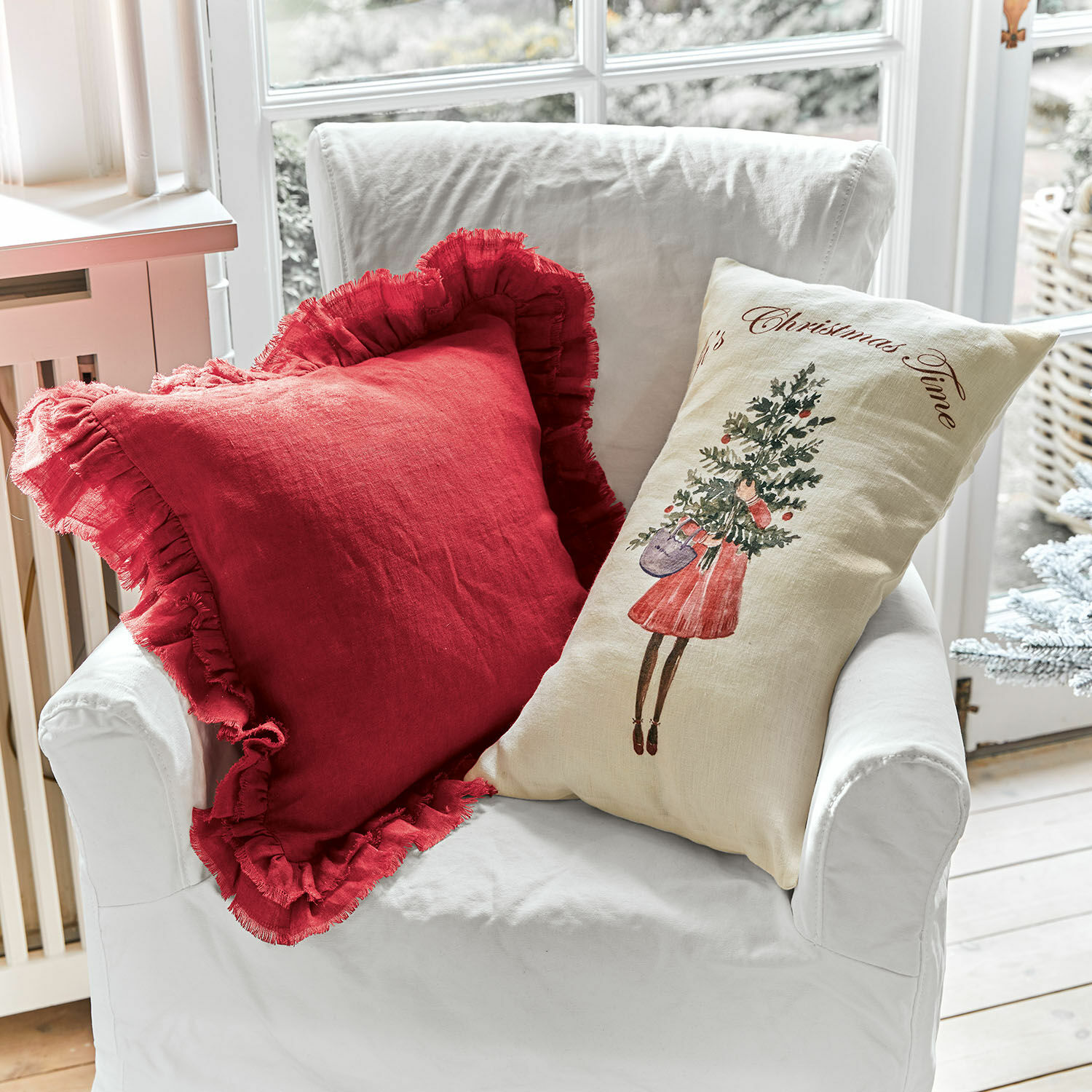 Lot de 2 housses de coussins Christmas Time Deux coussins décoratifs en lin sur un fauteuil blanc, rouge à volants et crème avec motif de Noël