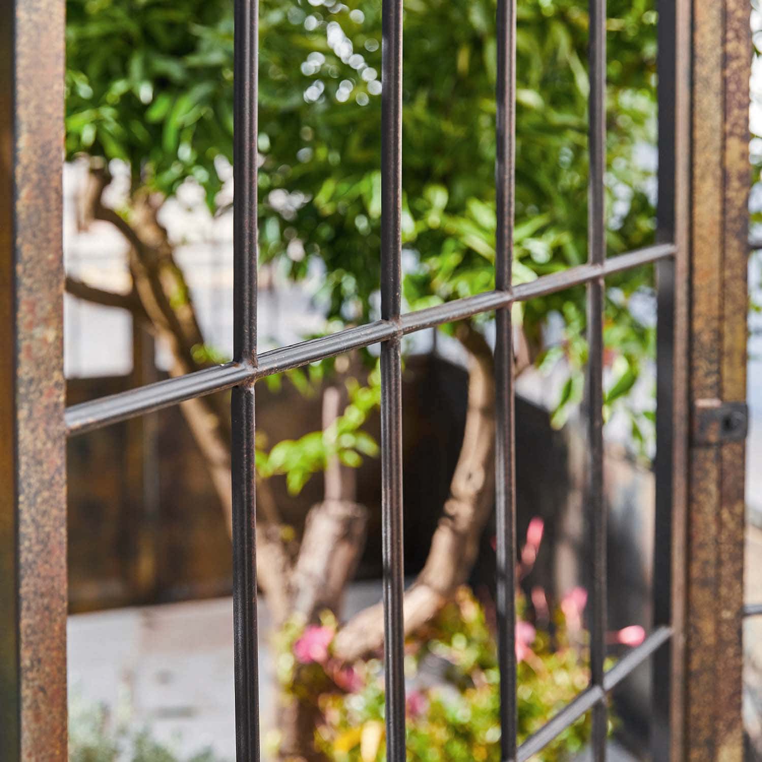 Grille métallique de jardin avec vue sur des plantes vertes et des fleurs en arrière-plan