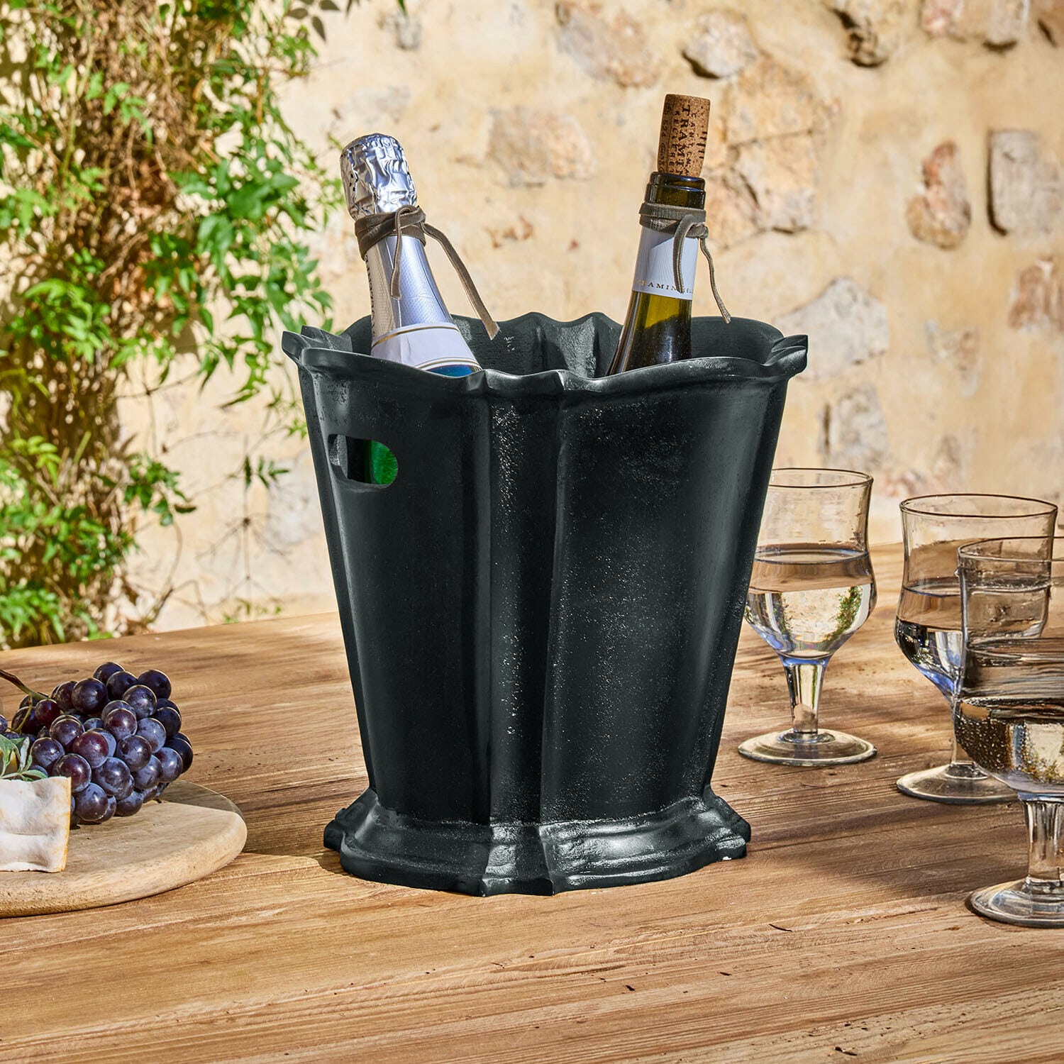 Seau à glace Trévaux Seau à glace en métal noir avec deux bouteilles de vin sur une table en bois en extérieur