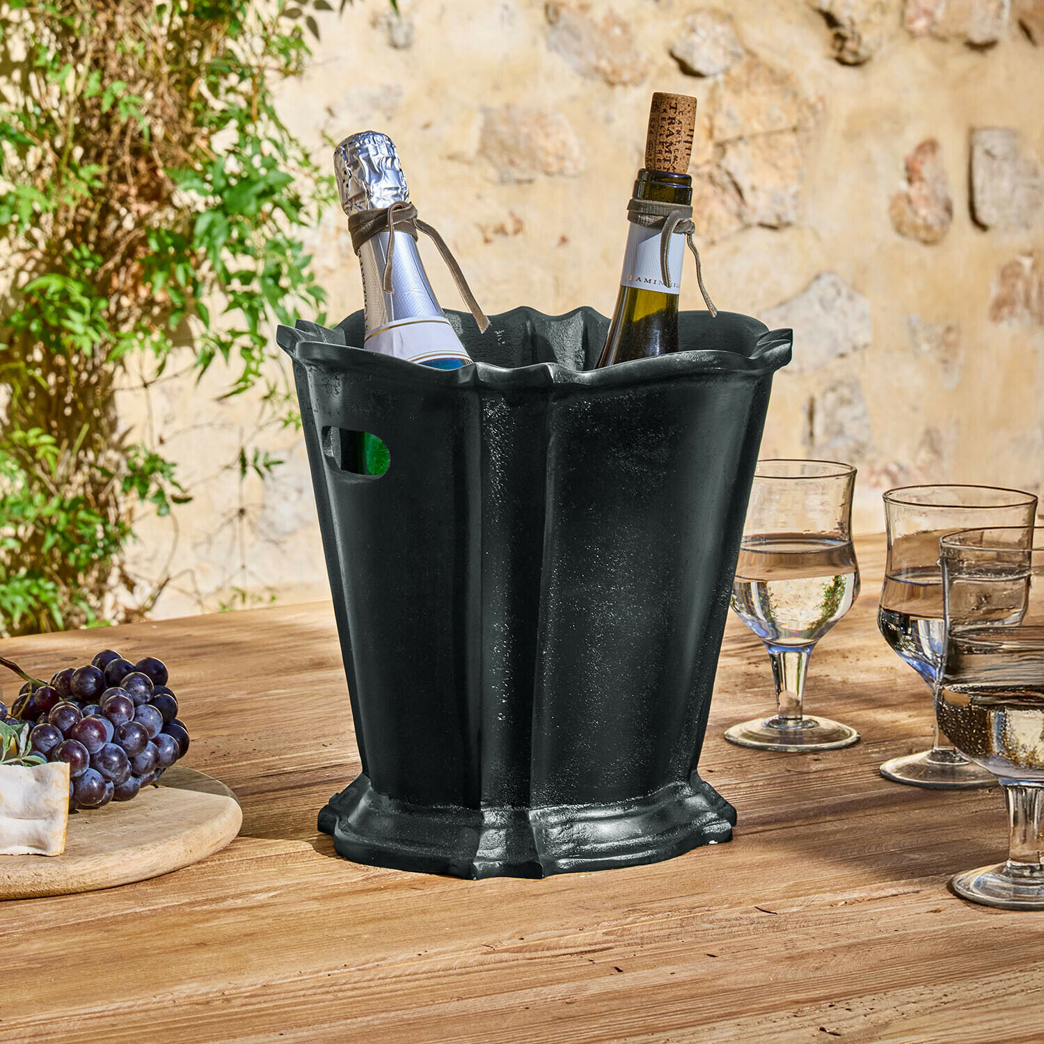 Seau à glace Trévaux Seau à glace en métal noir avec deux bouteilles de vin sur une table en bois en extérieur