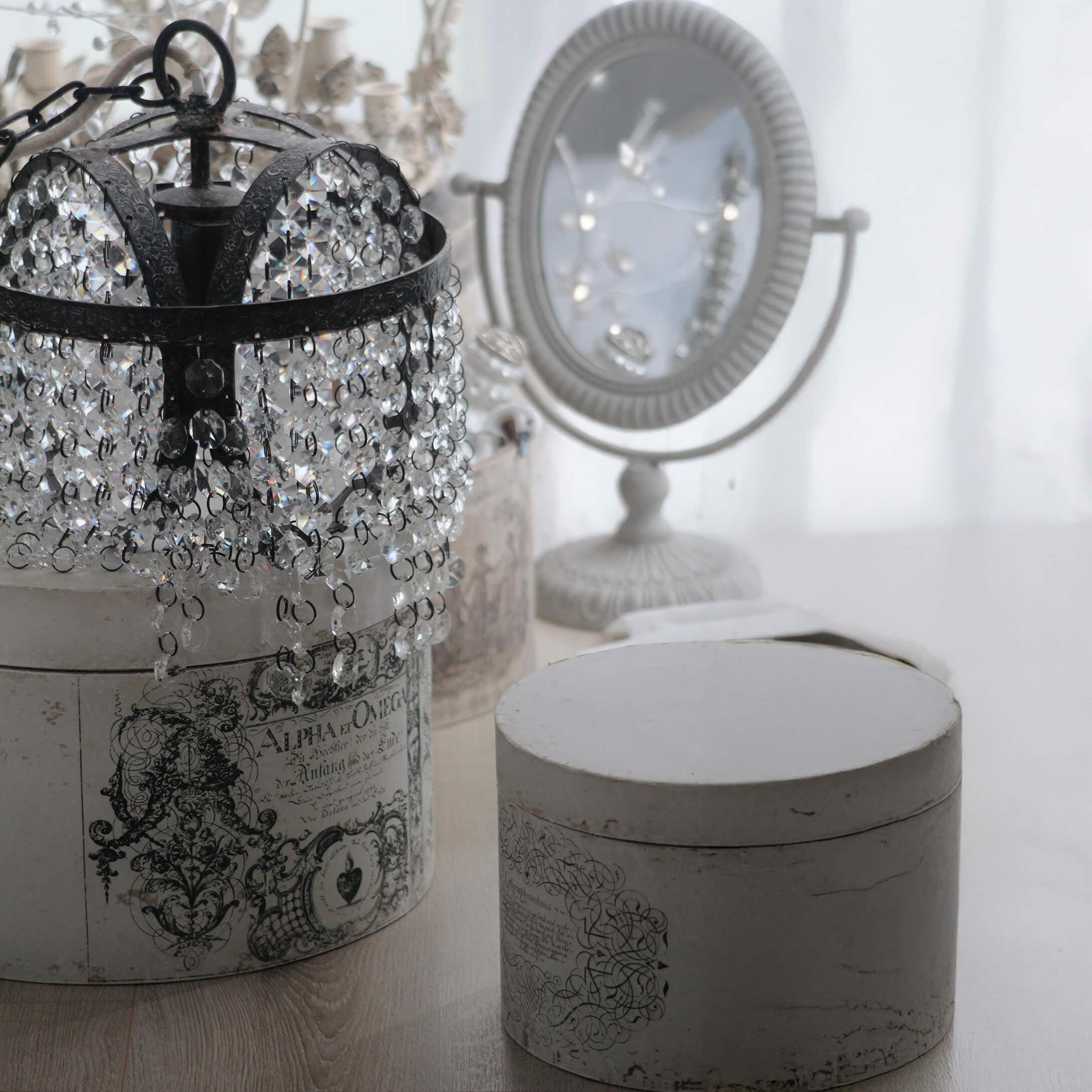 Lustre en cristal avec structure en métal noir posé sur une boîte vintage blanche décorée d'ornements