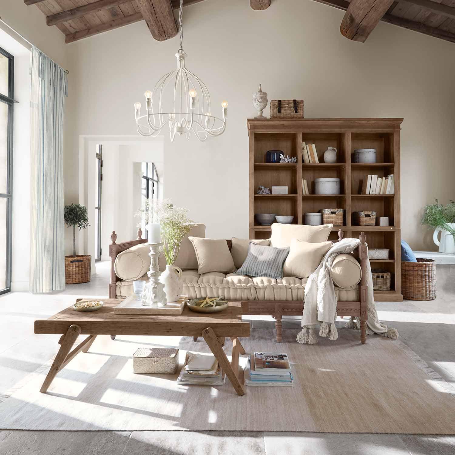 Salon chaleureux avec canapé en bois et coussins beige, table basse rustique en bois clair et étagère en arrière-plan