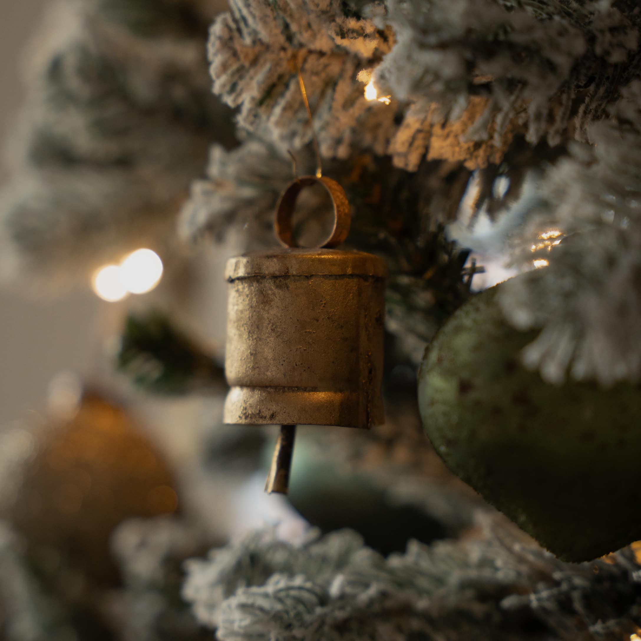 Clochette en métal doré suspendue à un sapin de Noël enneigé avec décorations festives