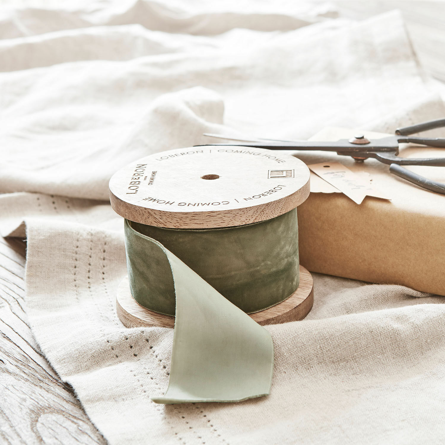 Ruban de velours Phaedra Ruban en velours vert sur bobine en bois posé sur tissu en lin avec ciseaux et paquet cadeau