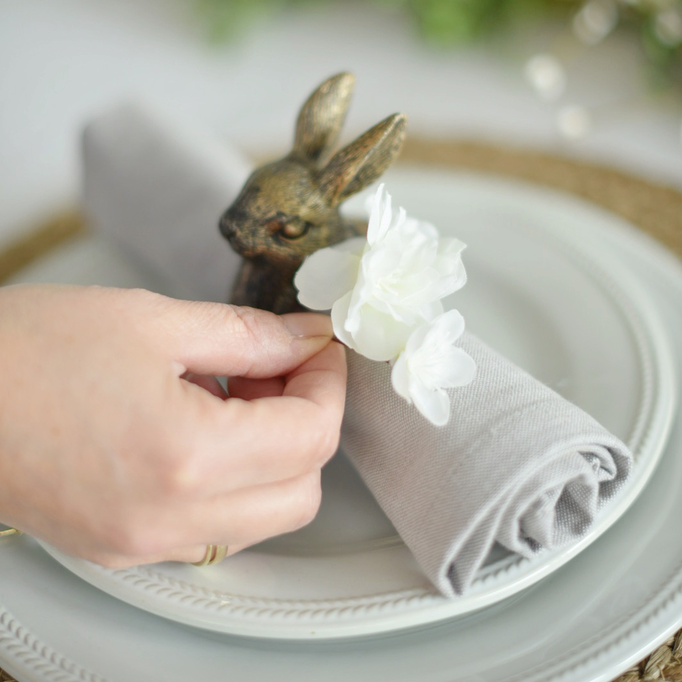 Rond de serviette en lin gris avec fleur blanche et décoration lapin en laiton sur assiette blanche