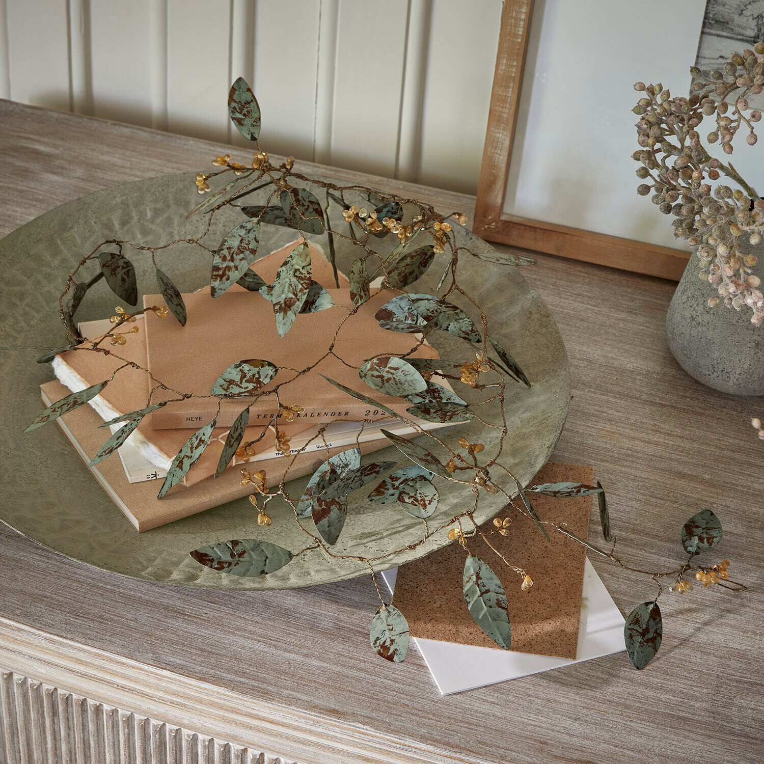 Guirlande Florivine Branche décorative en métal avec feuilles vertes et baies jaunes sur une table en bois avec des livres