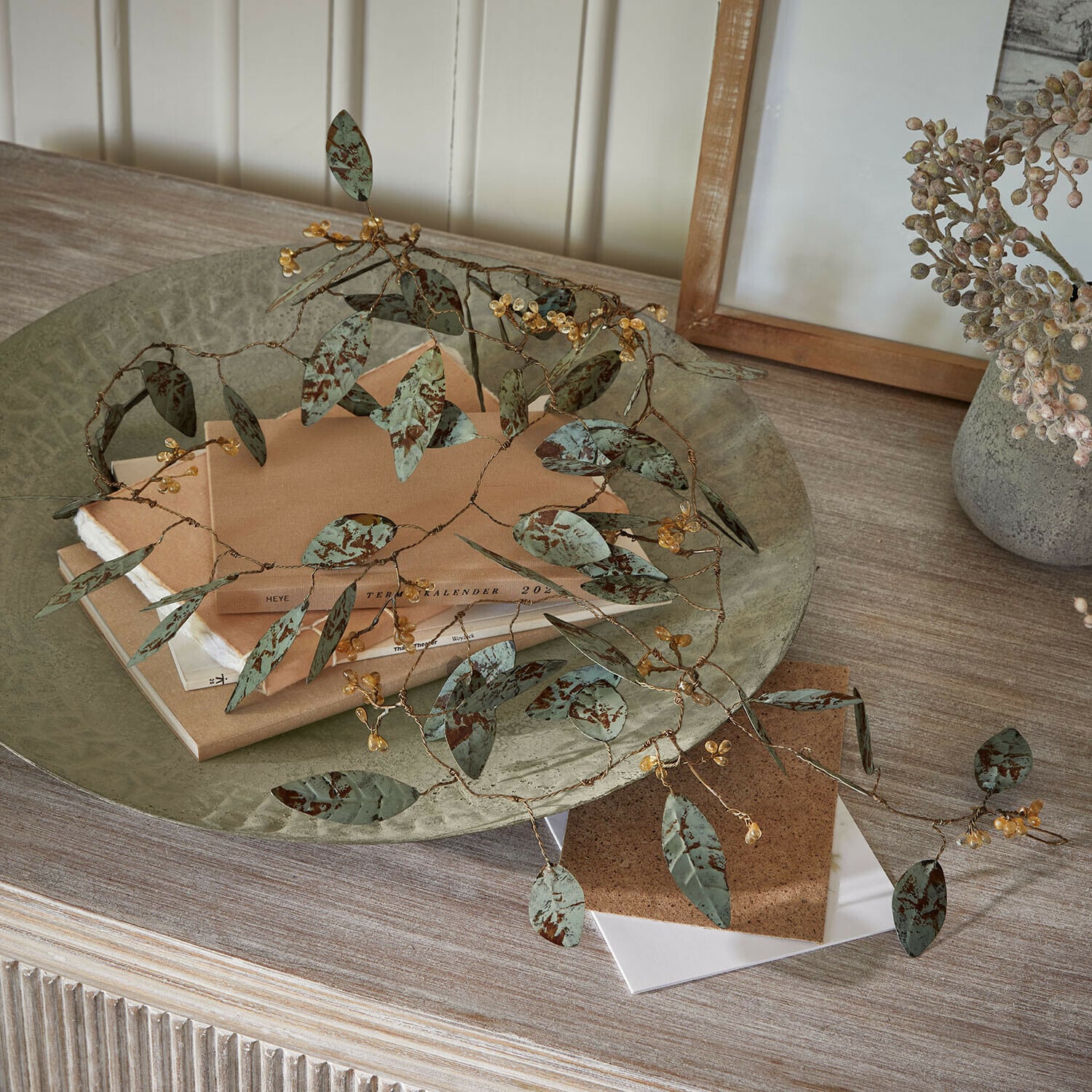 Guirlande Florivine Branche décorative en métal avec feuilles vertes et baies jaunes sur une table en bois avec des livres