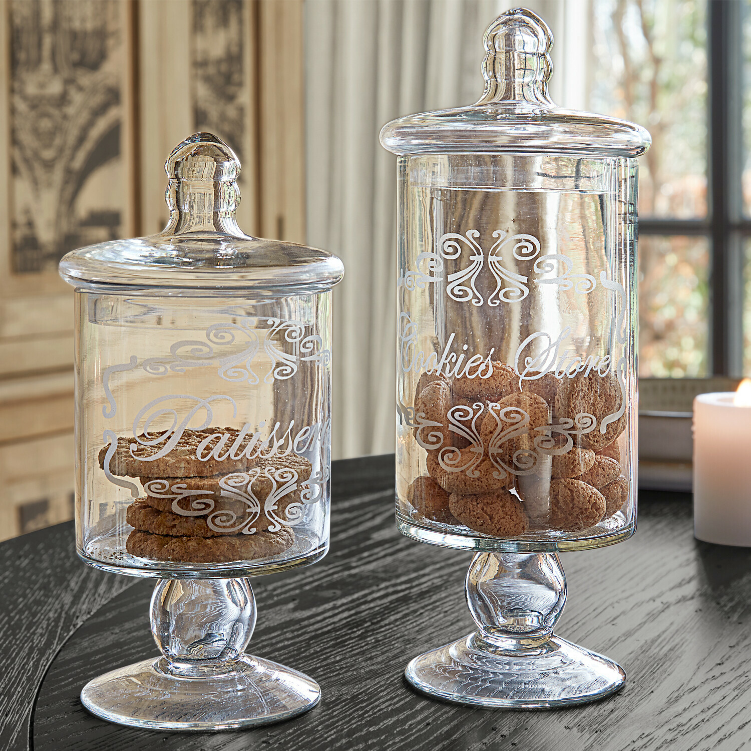 Lot de 2 bonbonnières Suzie Bocaux en verre avec couvercles et inscriptions décoratives remplis de biscuits sur une table noire