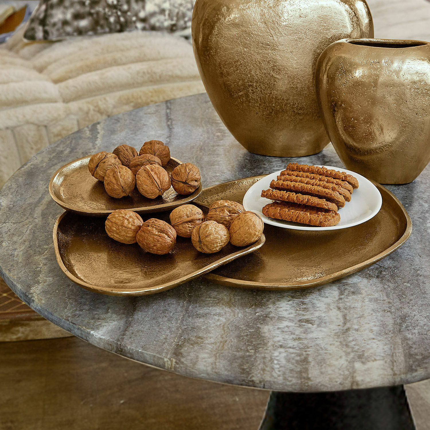 Coupe Zampillo Ensemble de plateaux et vases dorés en métal sur table en marbre avec noix et biscuits