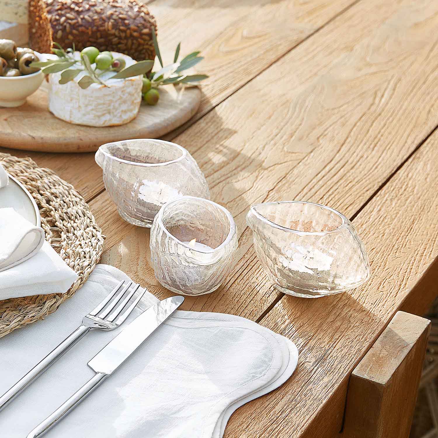 Ensemble de trois photophores en verre transparent à forme irrégulière sur une table en bois clair