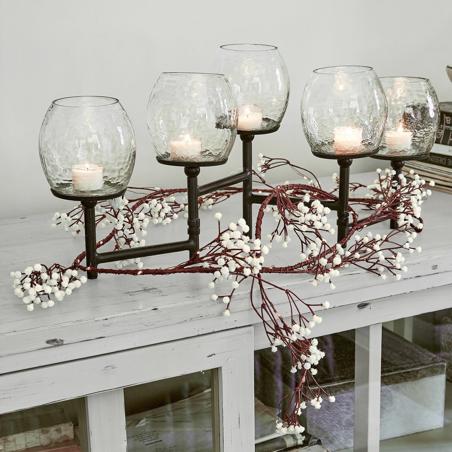 Guirlande lumineuse Fabrielle Bougeoir en métal avec cinq abat-jours en verre transparent et bougies blanches sur une table