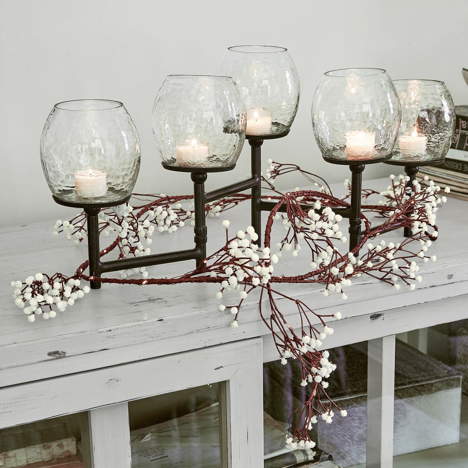 Guirlande lumineuse Fabrielle Bougeoir en métal avec cinq abat-jours en verre transparent et bougies blanches sur une table