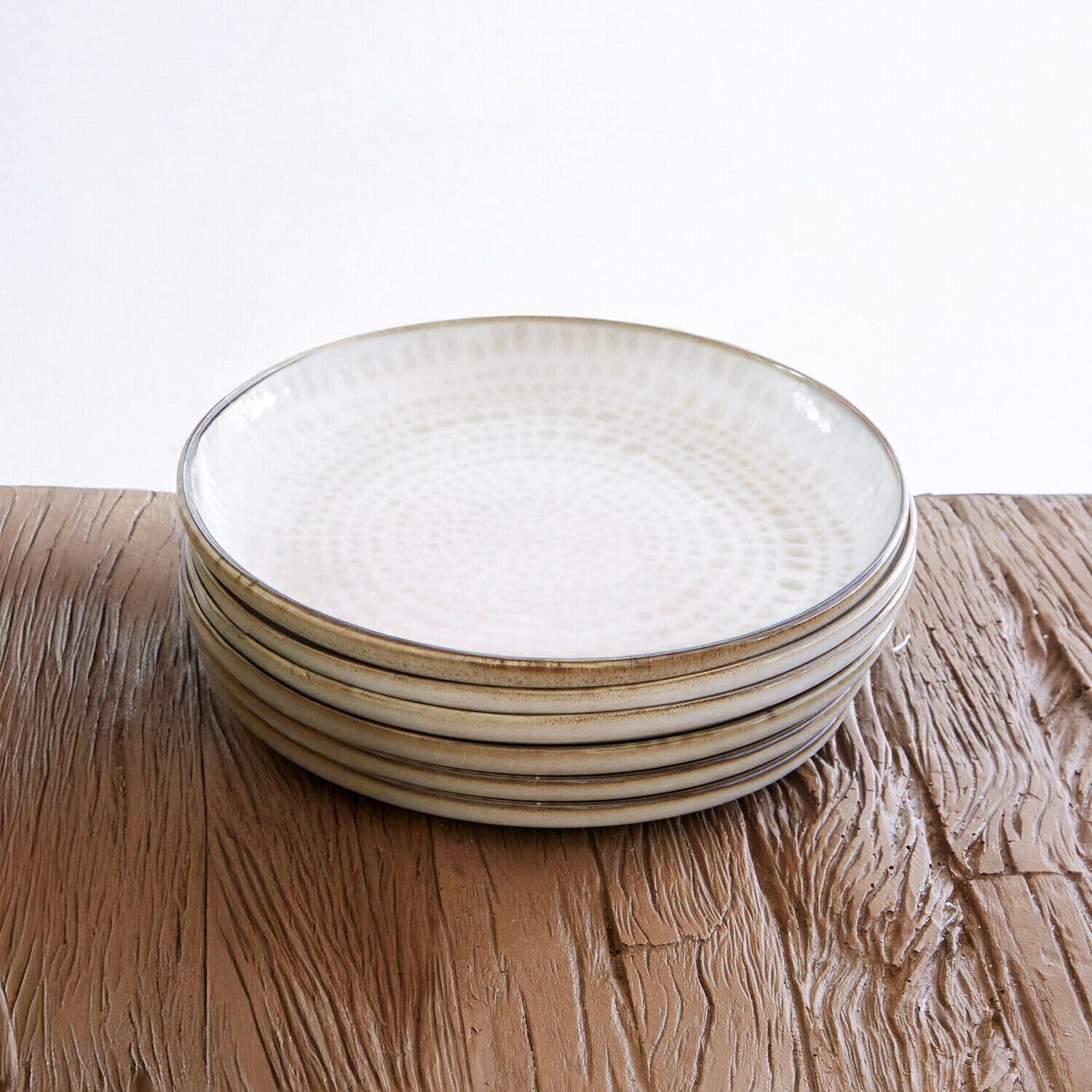 Lot de 6 assiettes Marnis Ensemble de six assiettes en céramique crème avec motif subtil, posées sur une table en bois