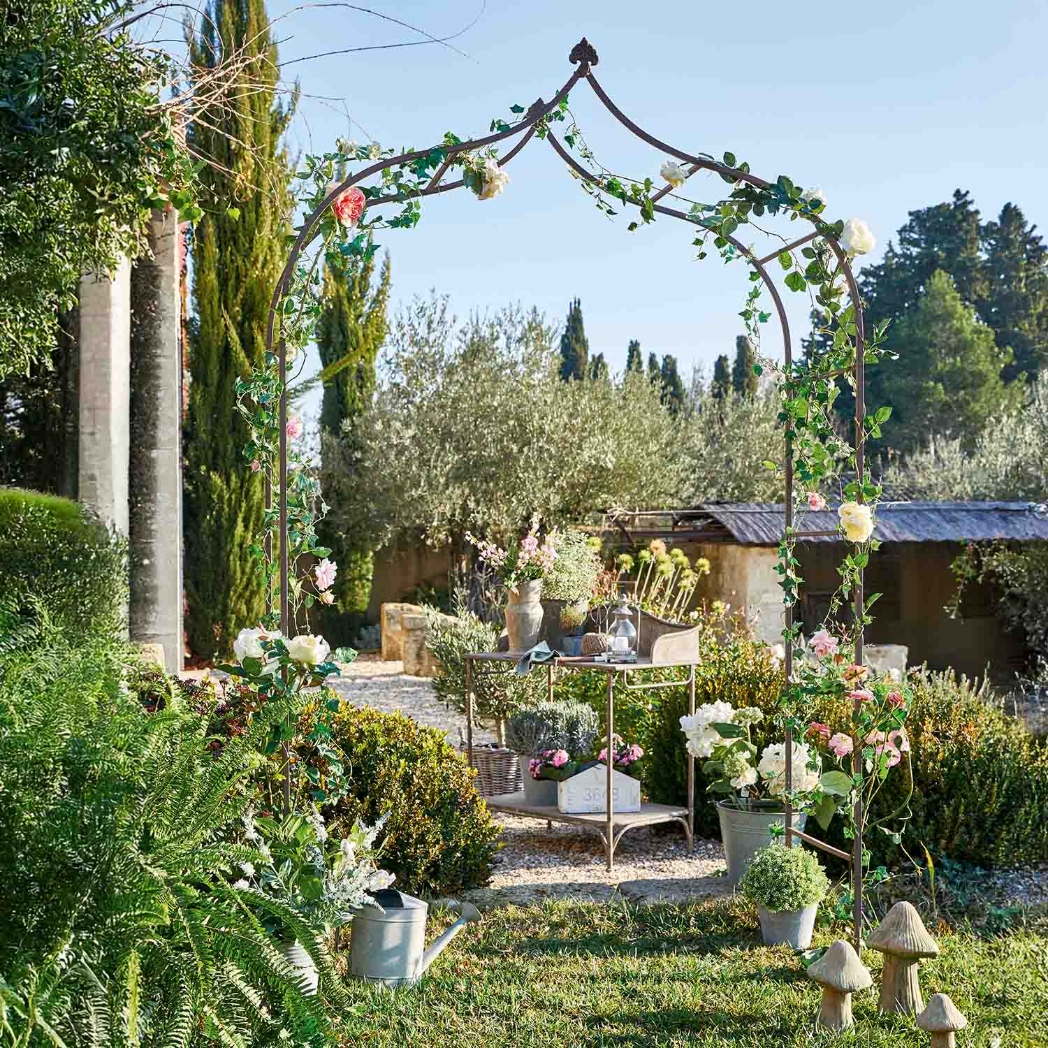 Pergola de jardin en métal avec feuillage vert et fleurs roses dans un jardin ensoleillé
