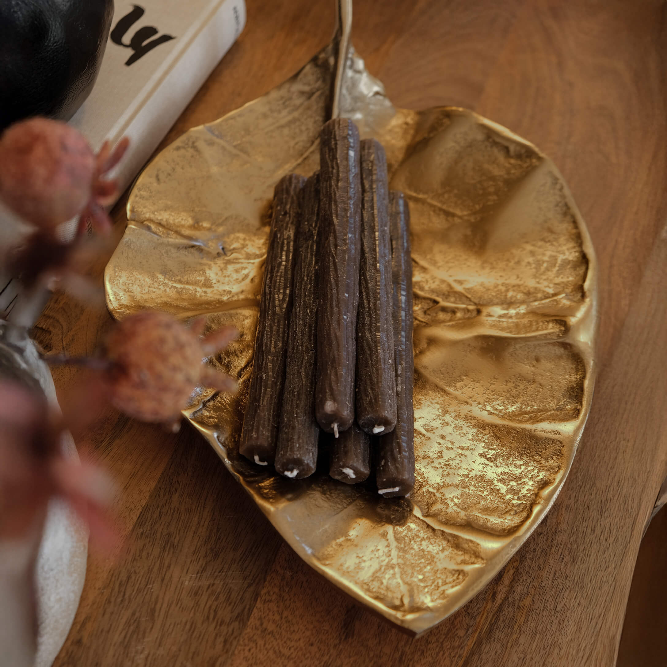 Plateau en métal doré en forme de feuille avec des bougies brunes décoratives sur une table en bois