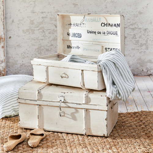 Coffres en bois blanc vieilli avec textiles rayés et pantoufles sur tapis en jute rustique