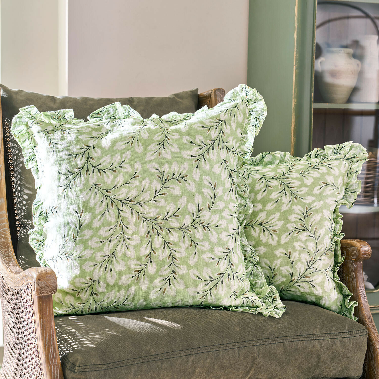 Coussins verts en coton avec motif feuilles blanches et volants sur les bords sur un fauteuil