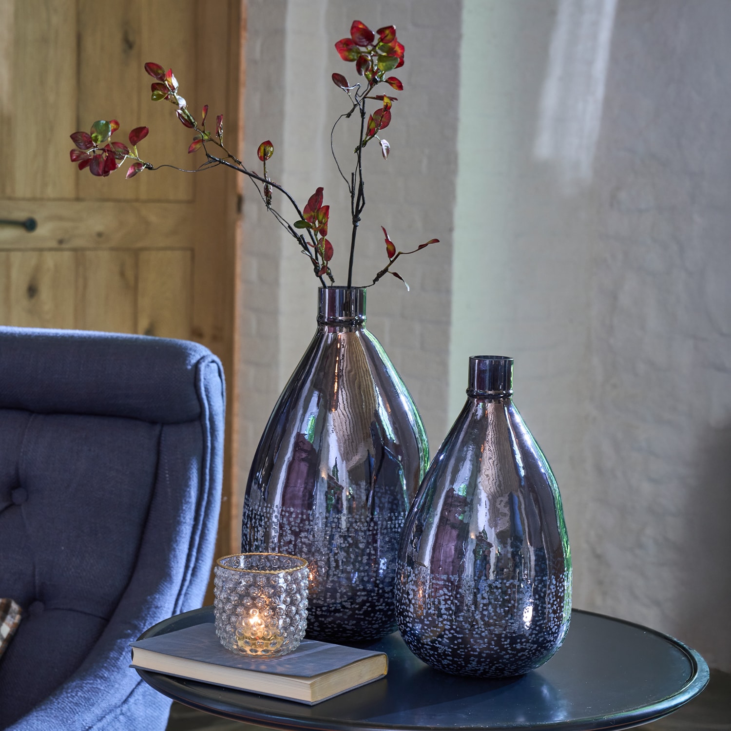 Deux vases décoratifs en verre gris foncé avec branches rouges sur une table avec bougeoir et livre
