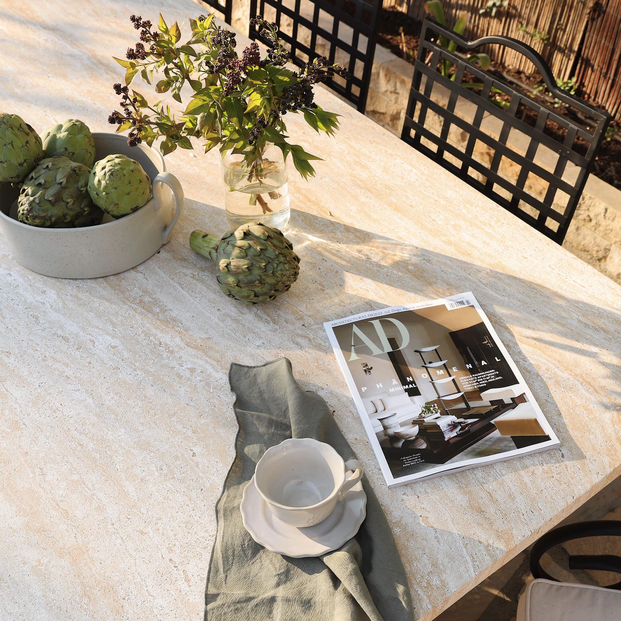 Table en pierre claire avec artichauts verts, tasse blanche et magazine de décoration en extérieur