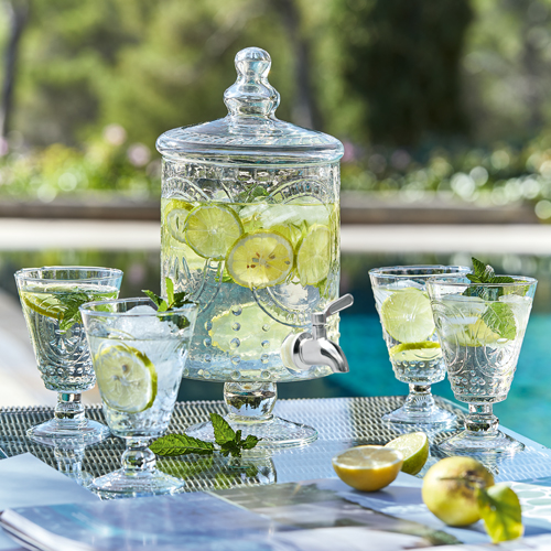 Distributeur en verre avec citron et menthe, quatre verres sur table extérieure près de la piscine