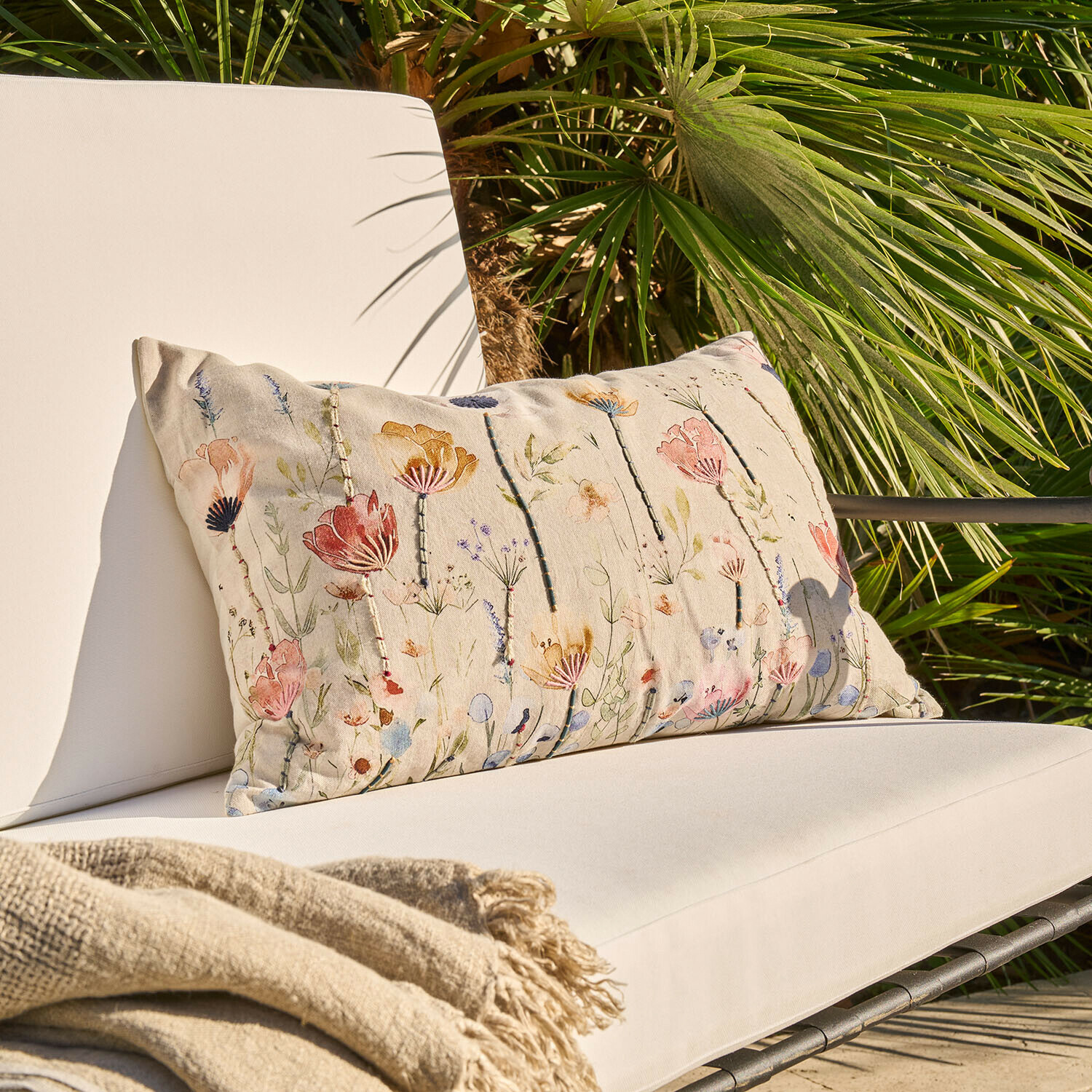 Coussin beige à motif floral sur fauteuil d'extérieur clair avec couverture beige