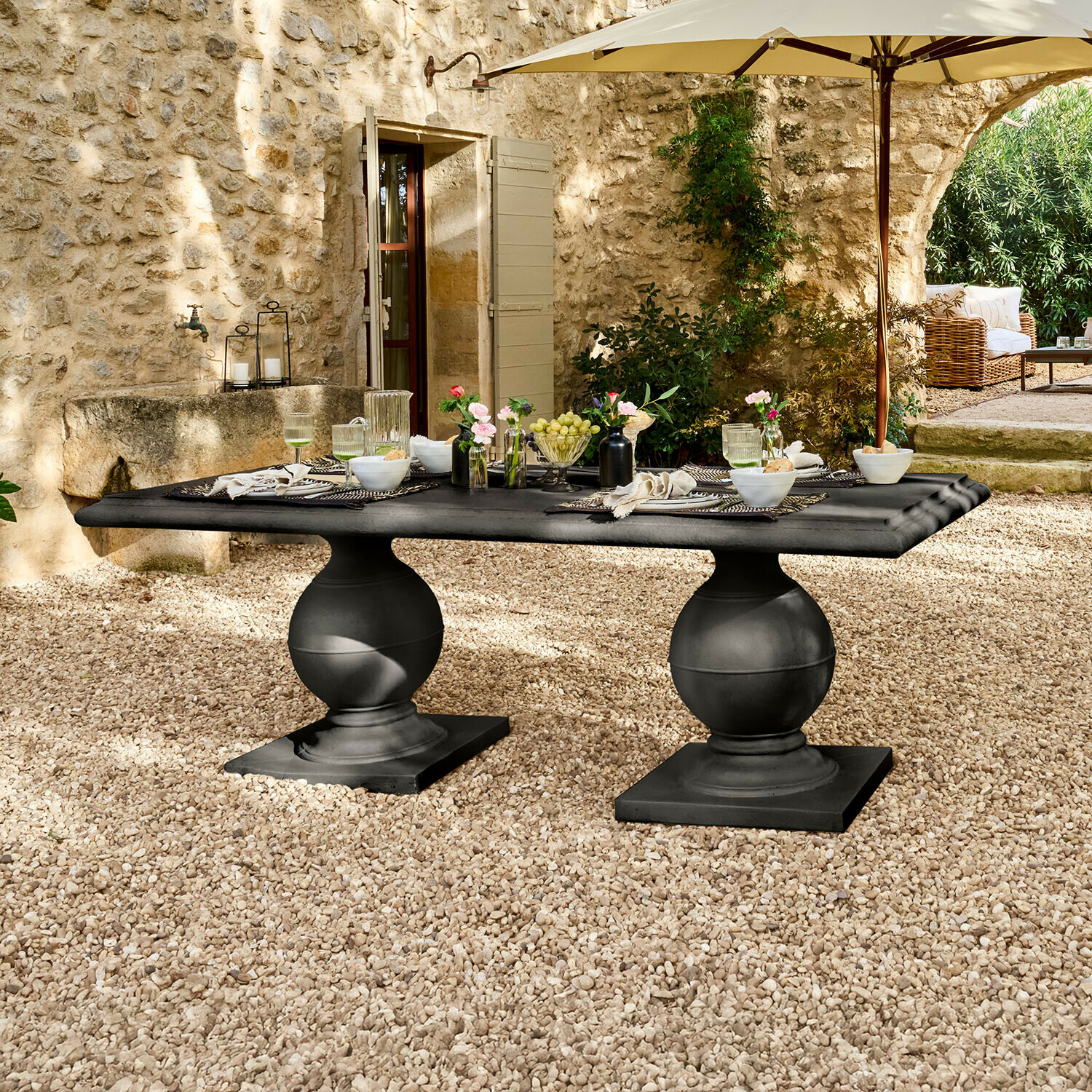 Table Talvero Table de jardin noire en pierre avec deux pieds sphériques sur patio en gravier sous parasol